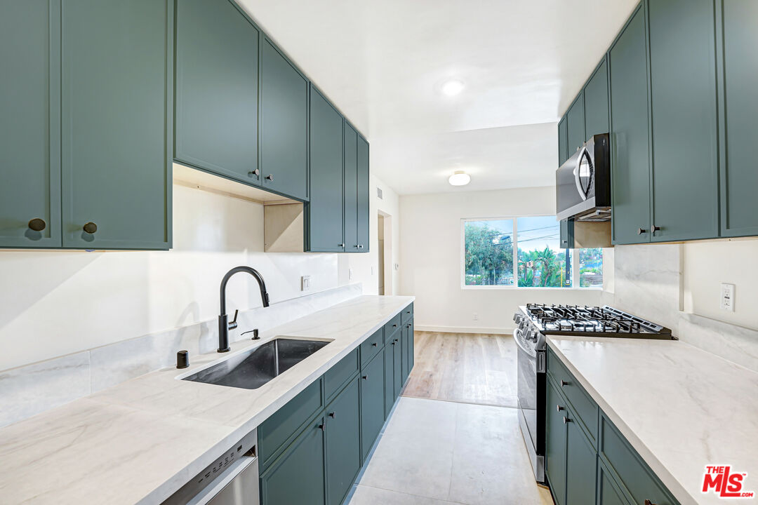 Galley kitchen with teal cabinets, white stone counters, and a window overlooking greenery.