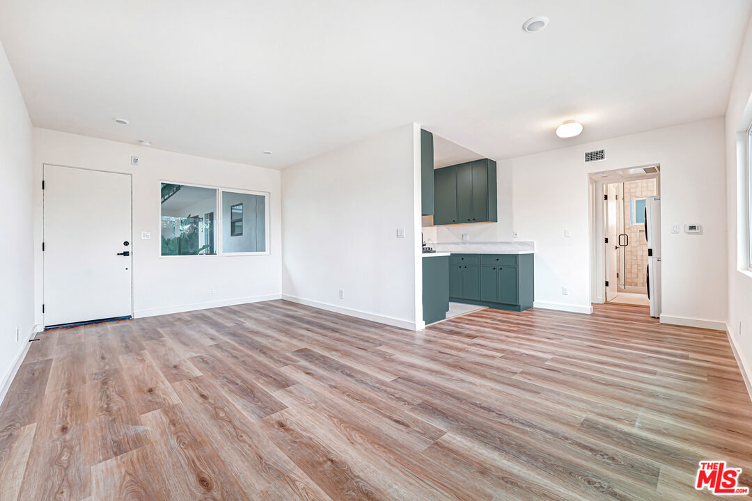 Vacant apartment interior with wood-look flooring and dark teal kitchen cabinets.