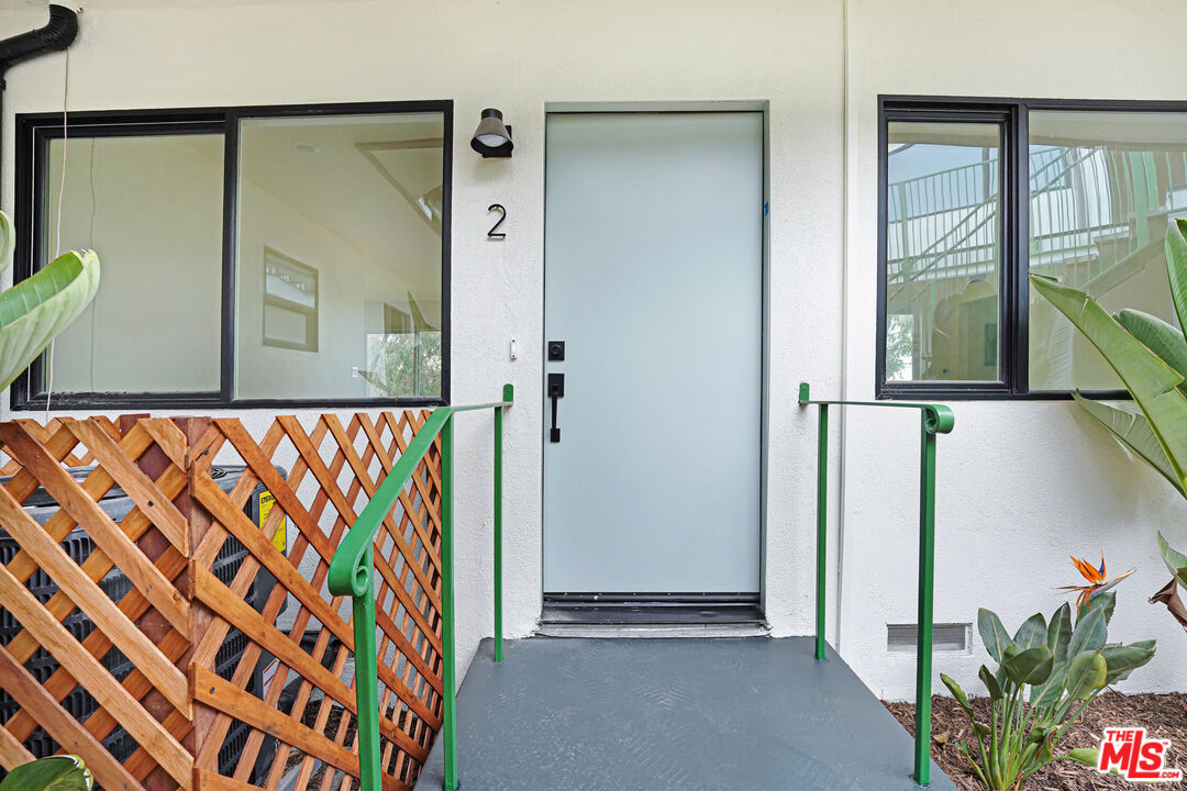 Unit 2 entrance with a pale blue door, green railings, and wooden lattice fence.