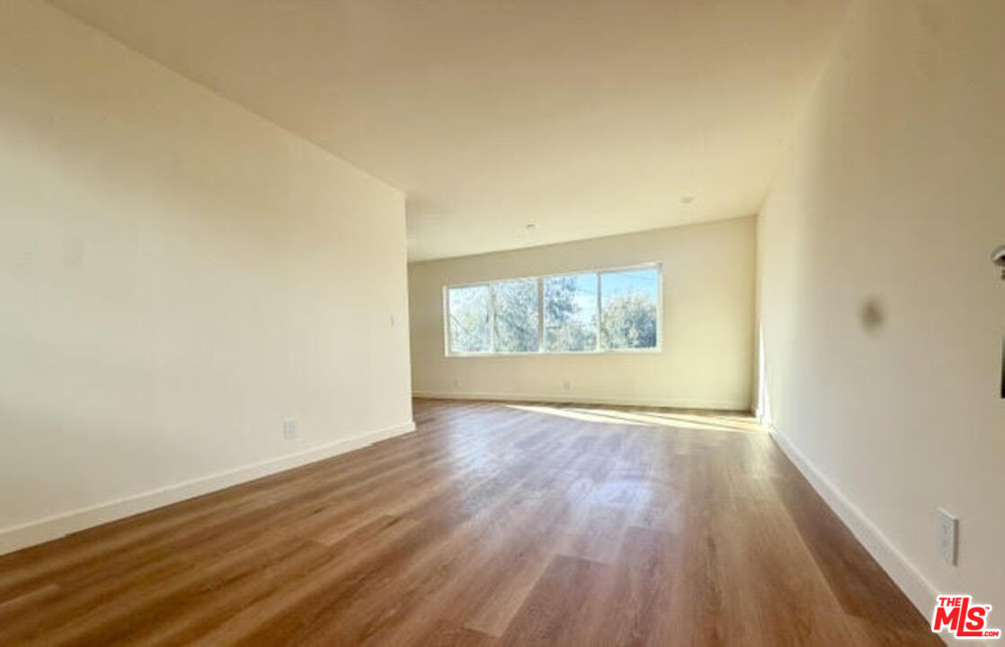 Empty living room with wood plank floors and a wide window overlooking trees.