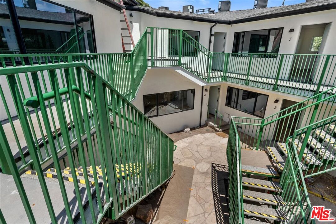 Apartment courtyard with green metal stairs and walkways surrounding a stone-paved central area.