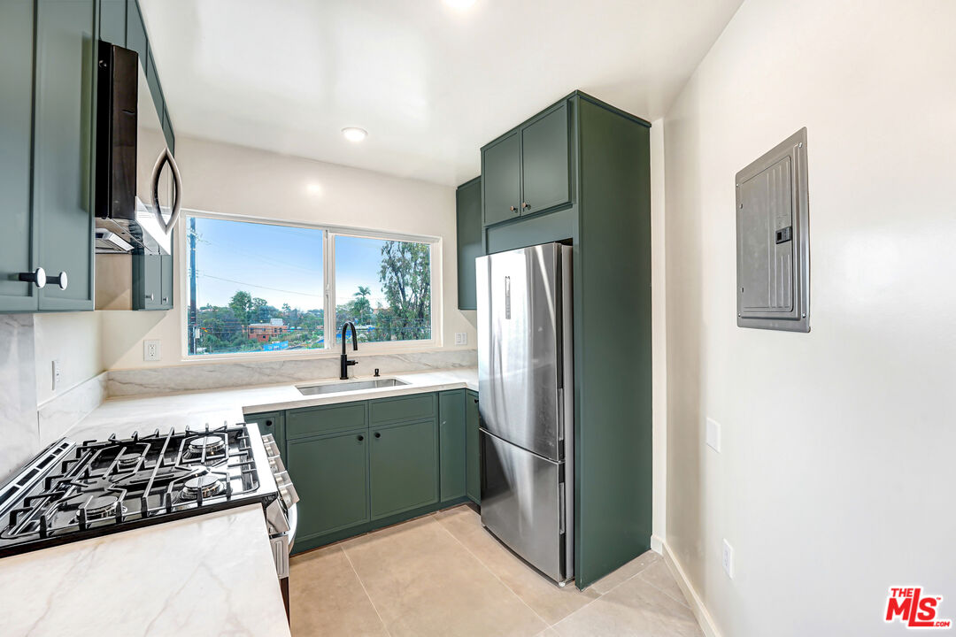 Kitchen with dark green cabinets, stainless steel appliances, and a wide window above the sink.