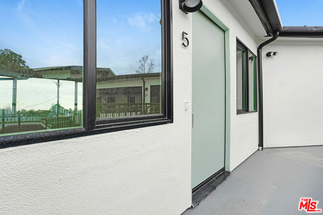 Unit 5 entrance with a pale green door, black-framed windows, and white stucco exterior.