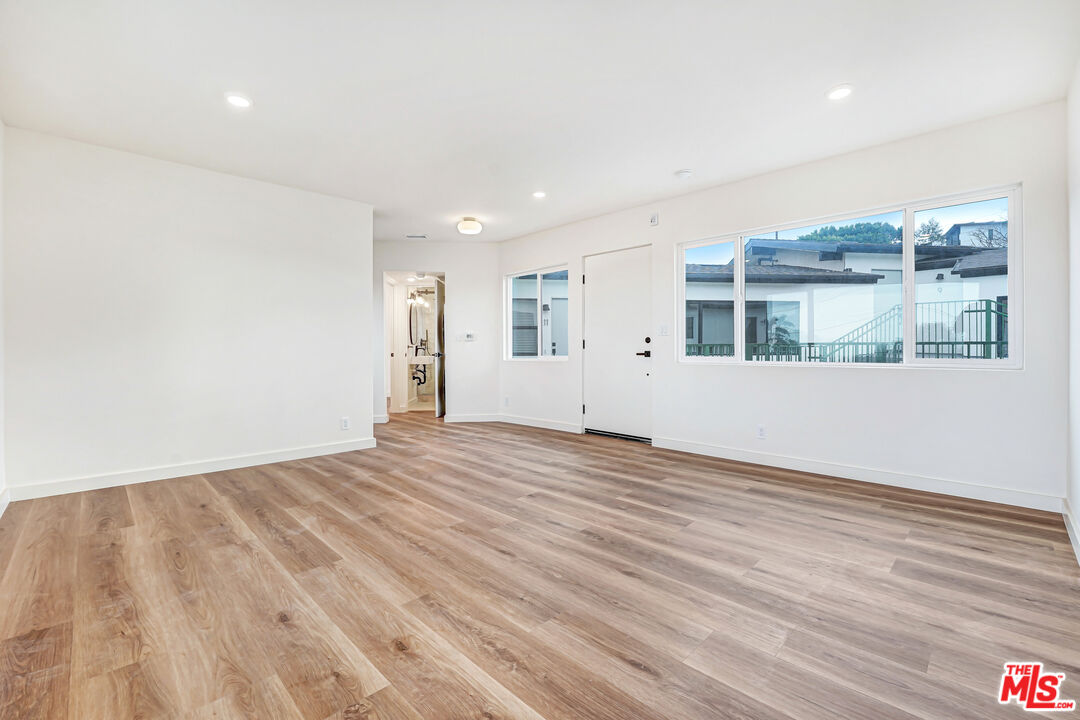 Empty living room with wide-plank wood flooring and large windows overlooking a neighboring building.