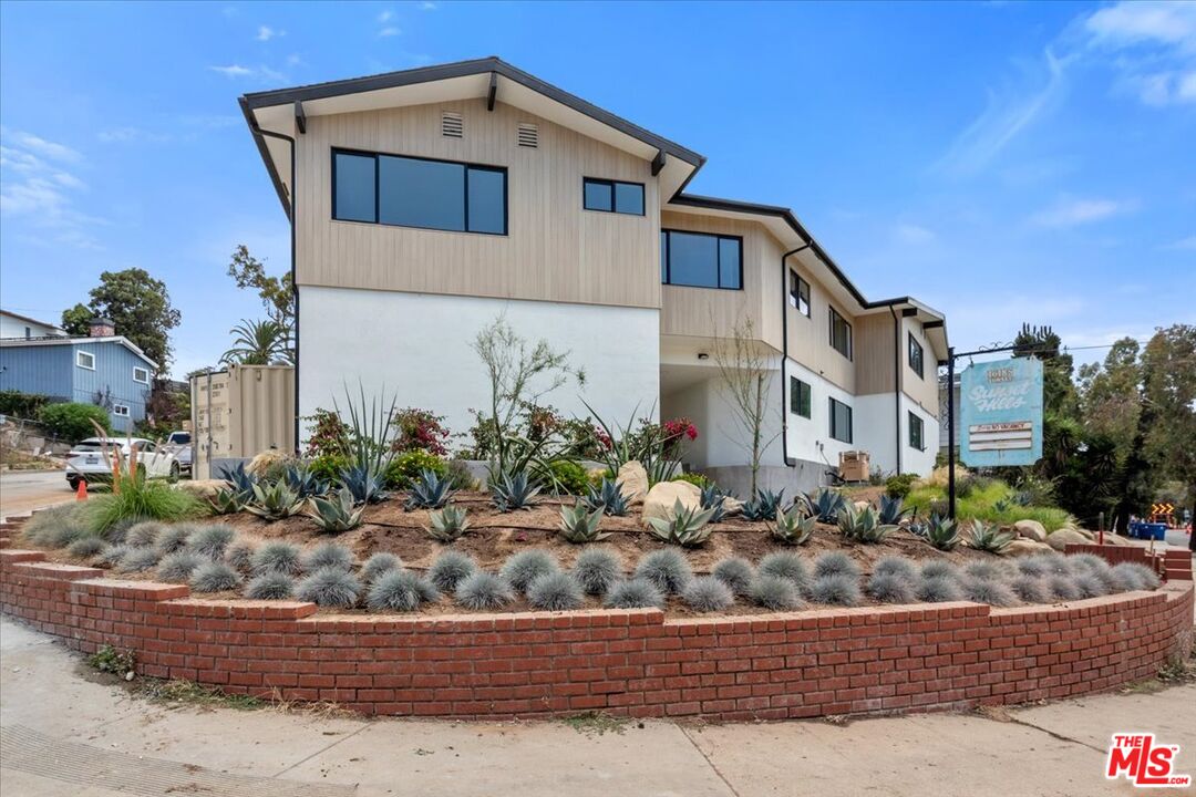 Modern multi-story building with beige siding, landscaped succulents, and a curved brick retaining wall.