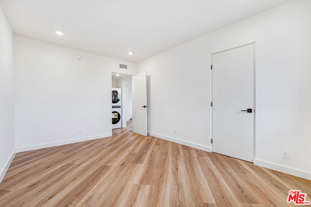 Empty room with wood-look flooring and a doorway to stacked laundry machines.