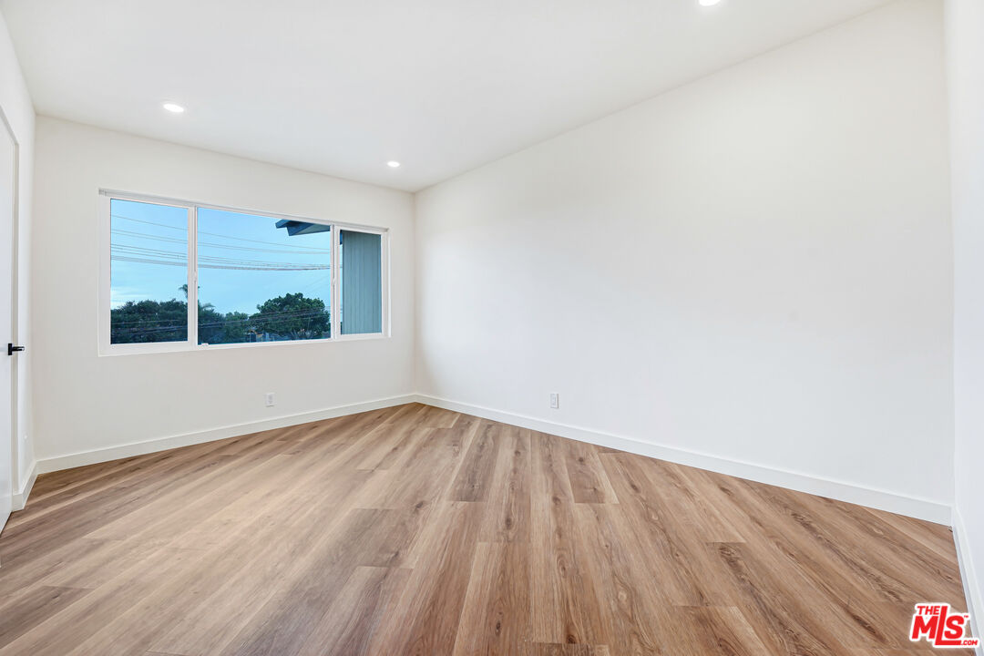 Empty room with warm wood-plank flooring, white walls, and a wide window.