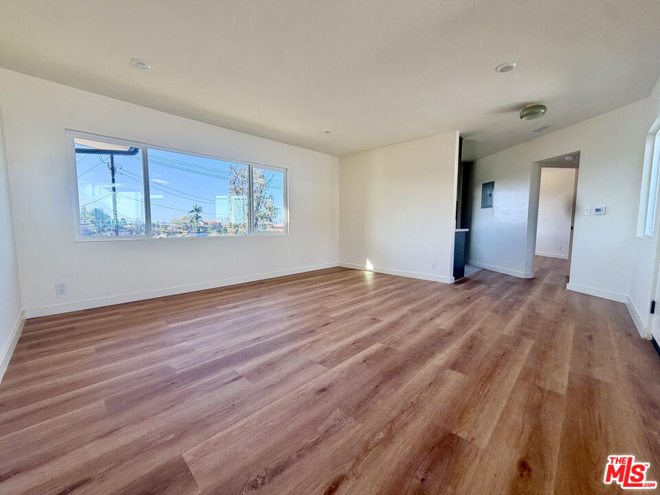 Vacant room with wide-plank wood floors and a large window overlooking nearby homes.