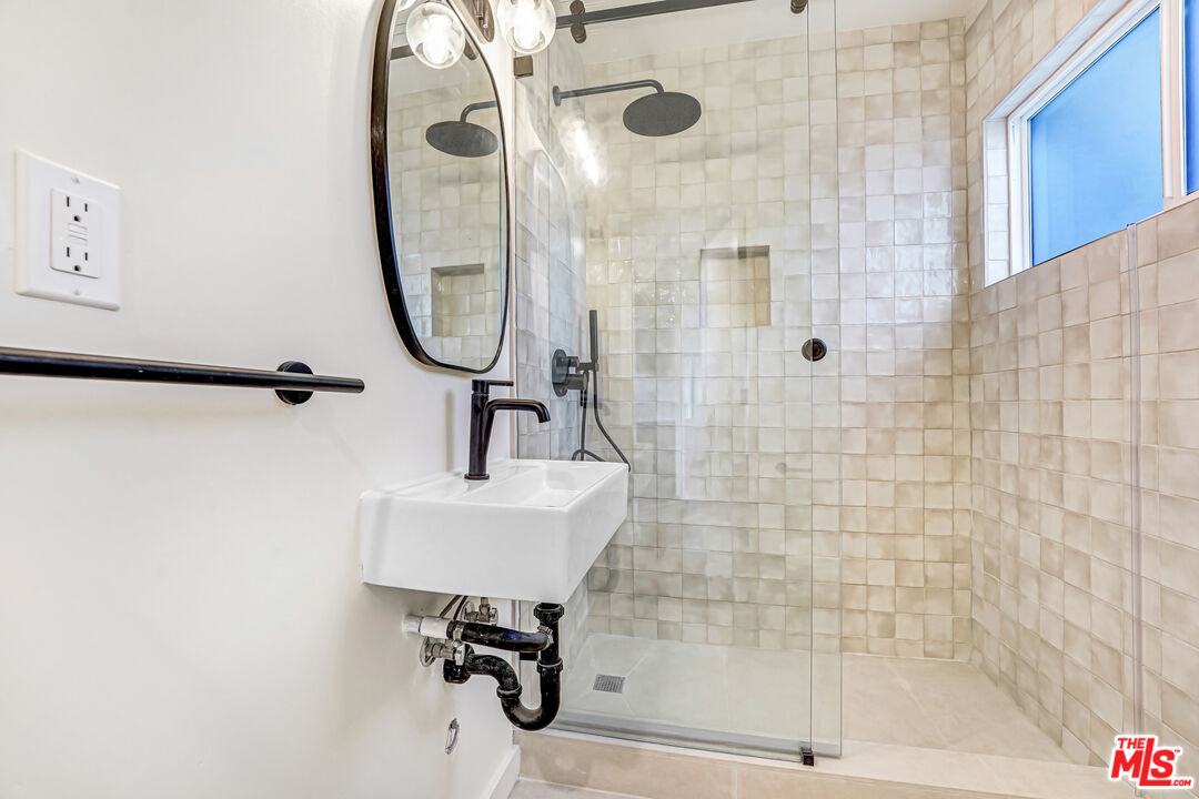 Bathroom with a glass-enclosed tiled shower, high window, and wall-mounted sink.