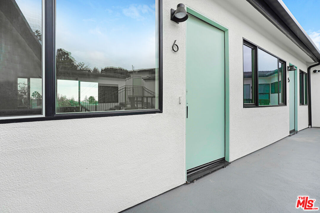 Building exterior with mint-green unit 6 door, black-framed windows, and a gray walkway.