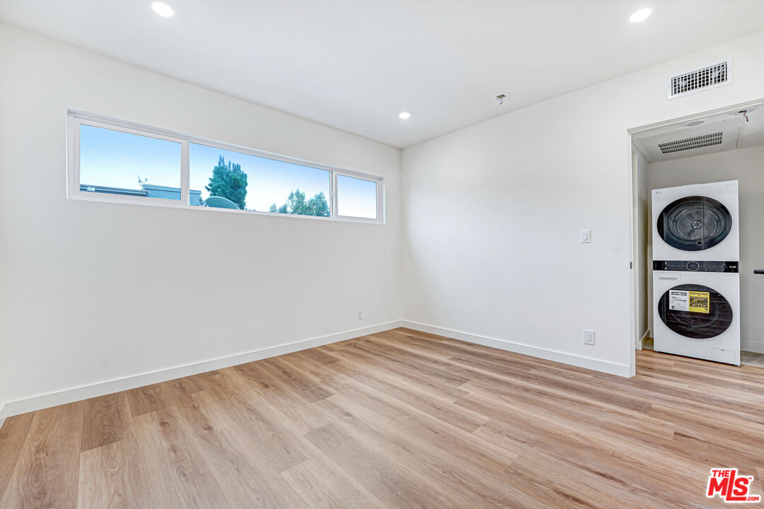 Empty room with wood-look floors, high windows, and washer and dryer in an alcove.