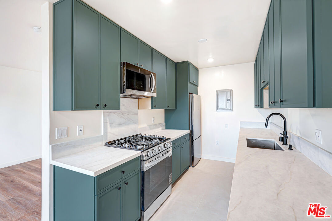 Kitchen with teal-green cabinets, marble-look counters, stainless steel appliances, and a gas range.
