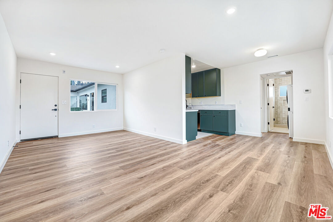 Vacant apartment interior with dark green kitchen cabinets and light wood-look flooring.
