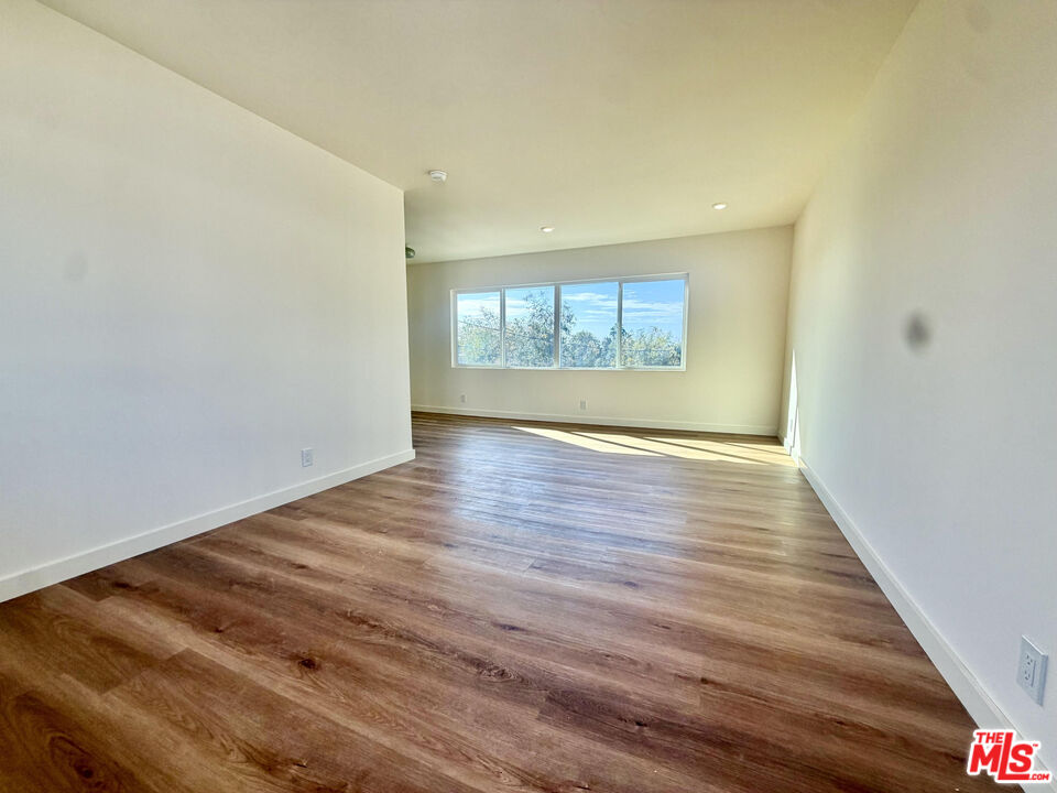 Empty room with wood flooring and a wide window overlooking trees.