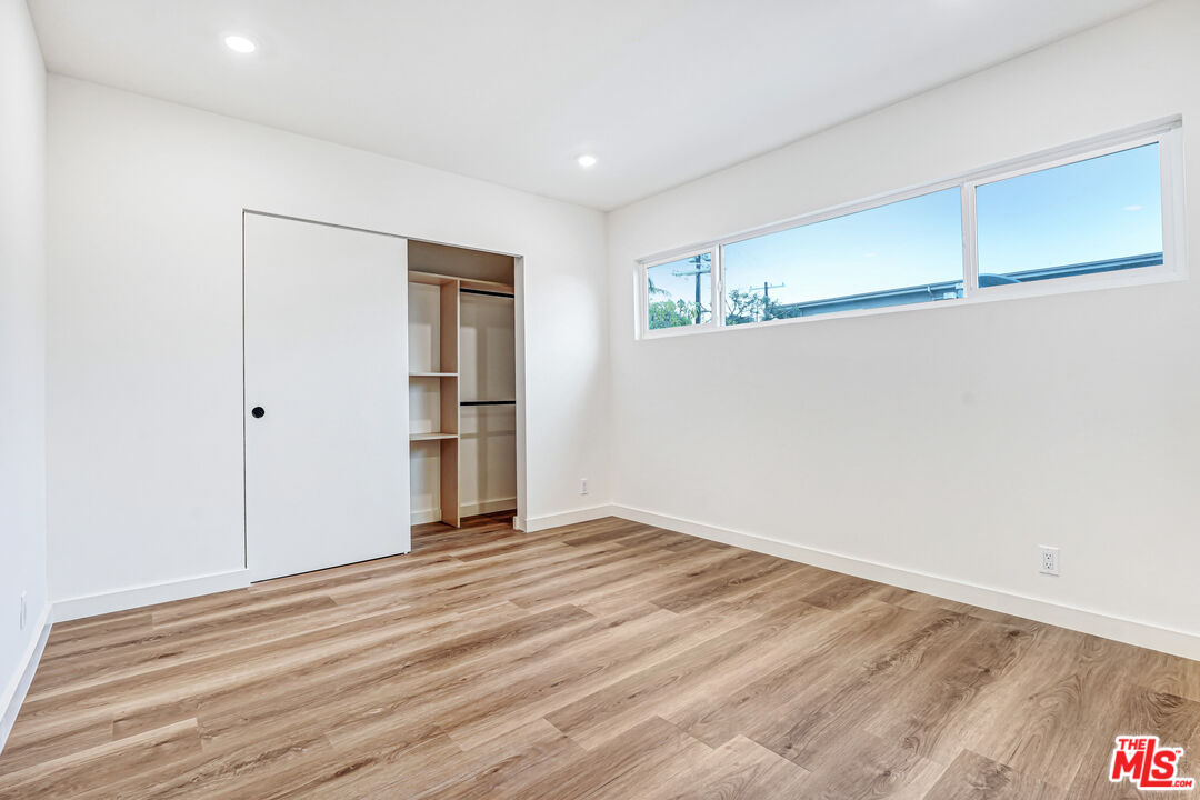 Vacant bedroom with wood-look flooring, an open closet, and a high horizontal window.
