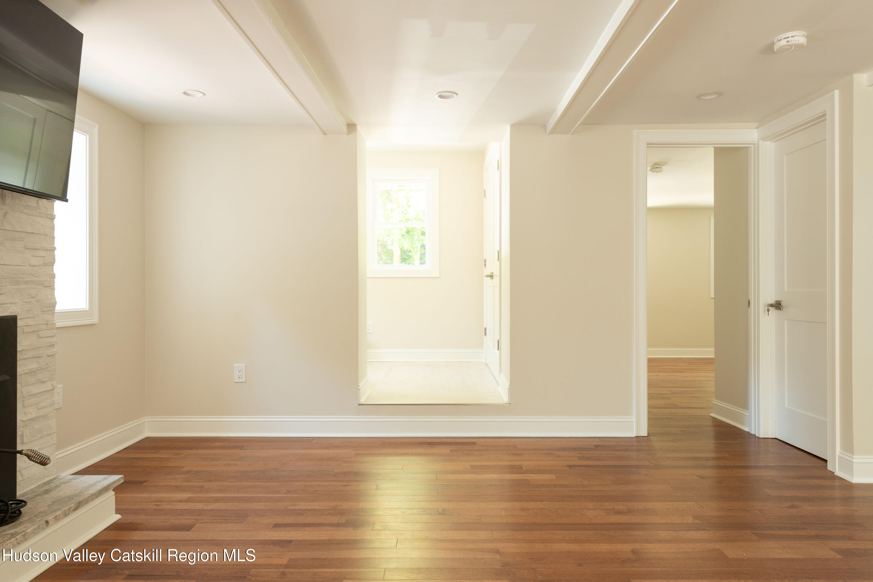 Unfurnished living room with hardwood floors, a stone fireplace, and open doorways.