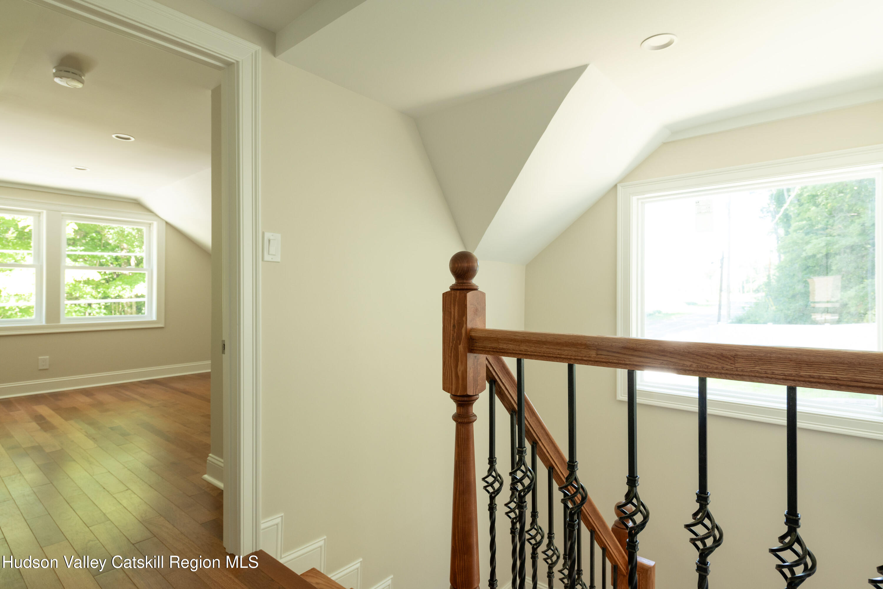 Staircase landing with a wooden handrail, wrought-iron balusters, and a large window.