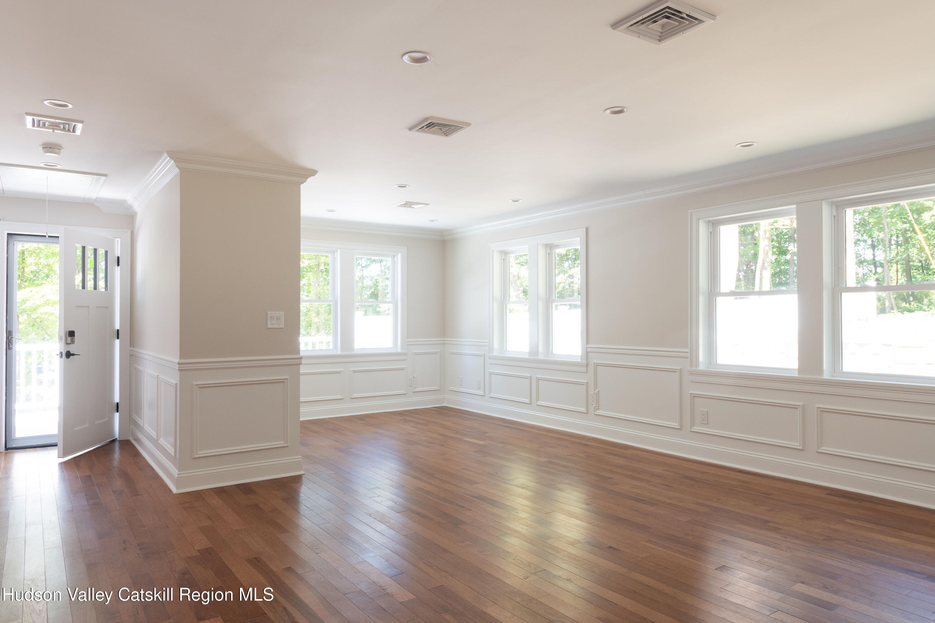 Empty room with hardwood floors, white paneled walls, and large windows.