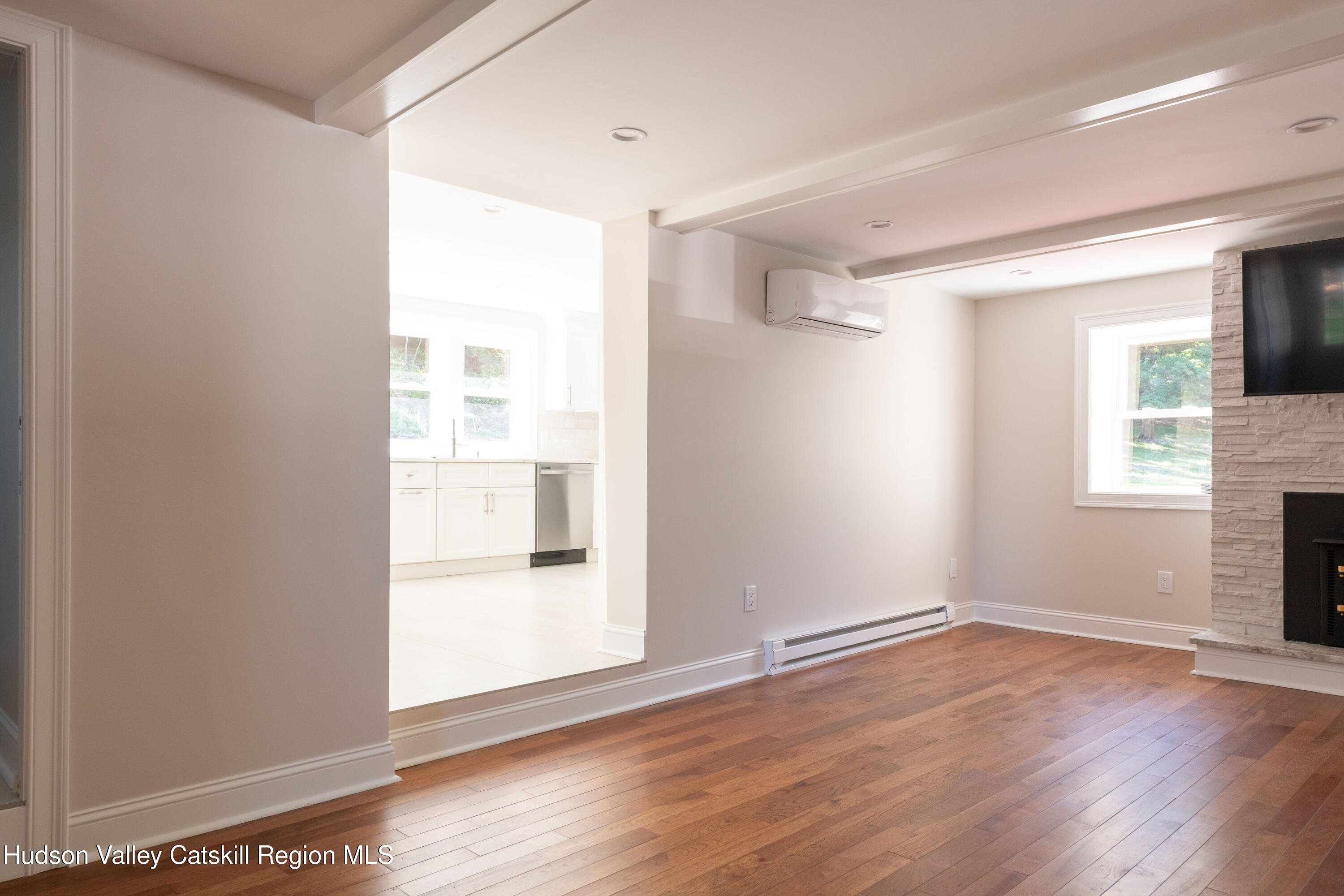 Living room with hardwood floors, stone fireplace, and an open view into the white kitchen.