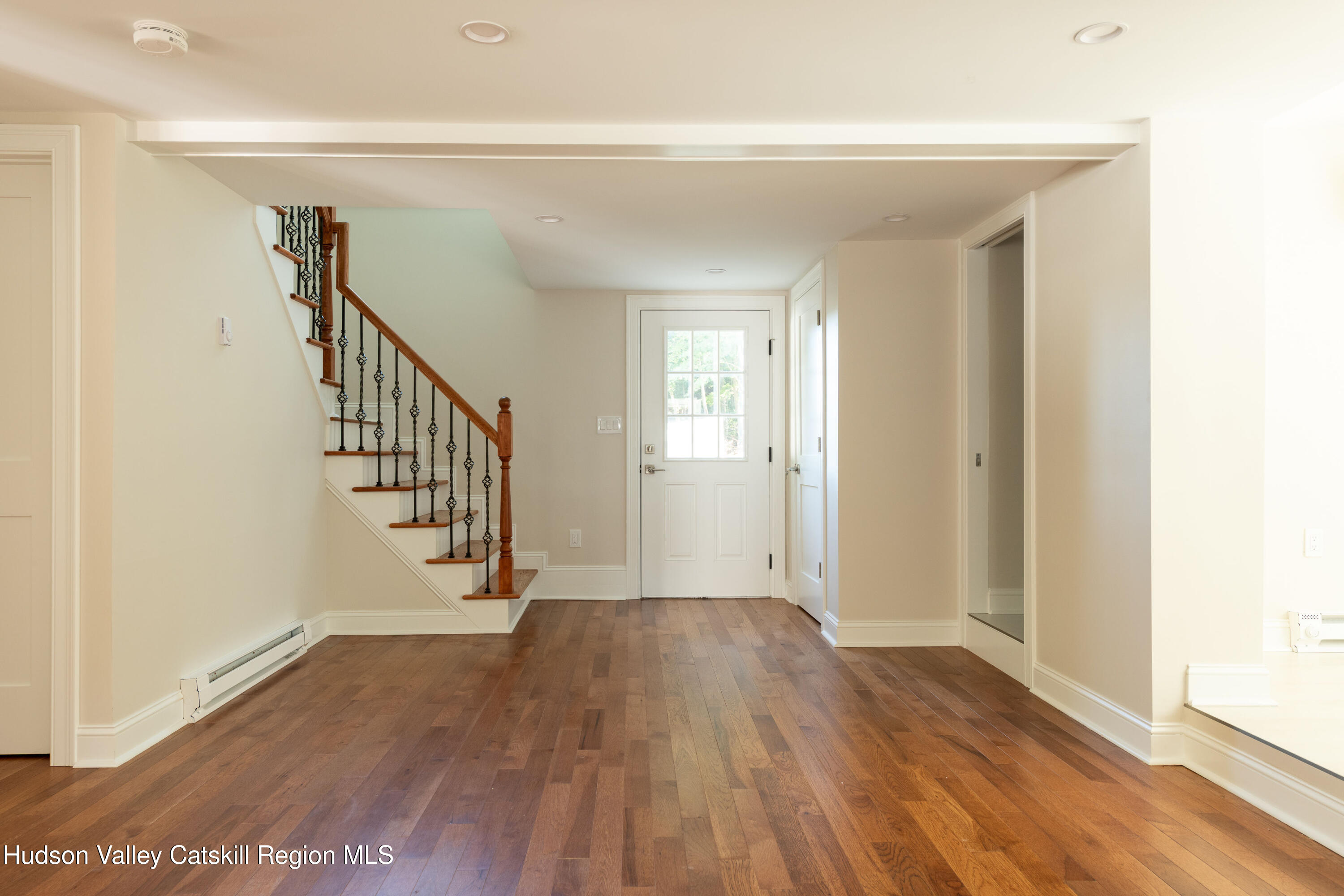 Entry hall with hardwood floors, a staircase, and a glass-paneled front door.