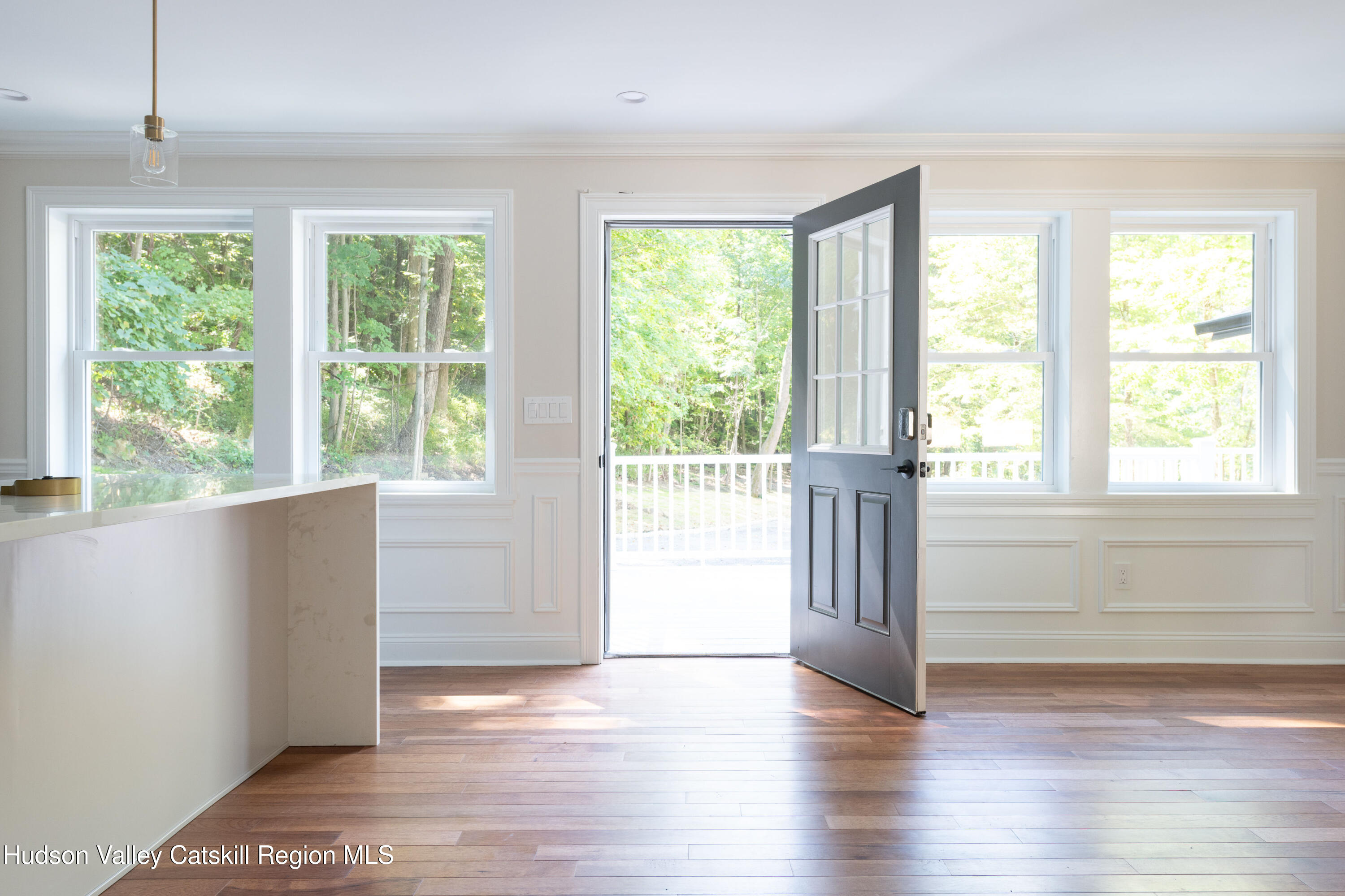 Bright entry with hardwood floors, paneled walls, and an open front door facing leafy trees.
