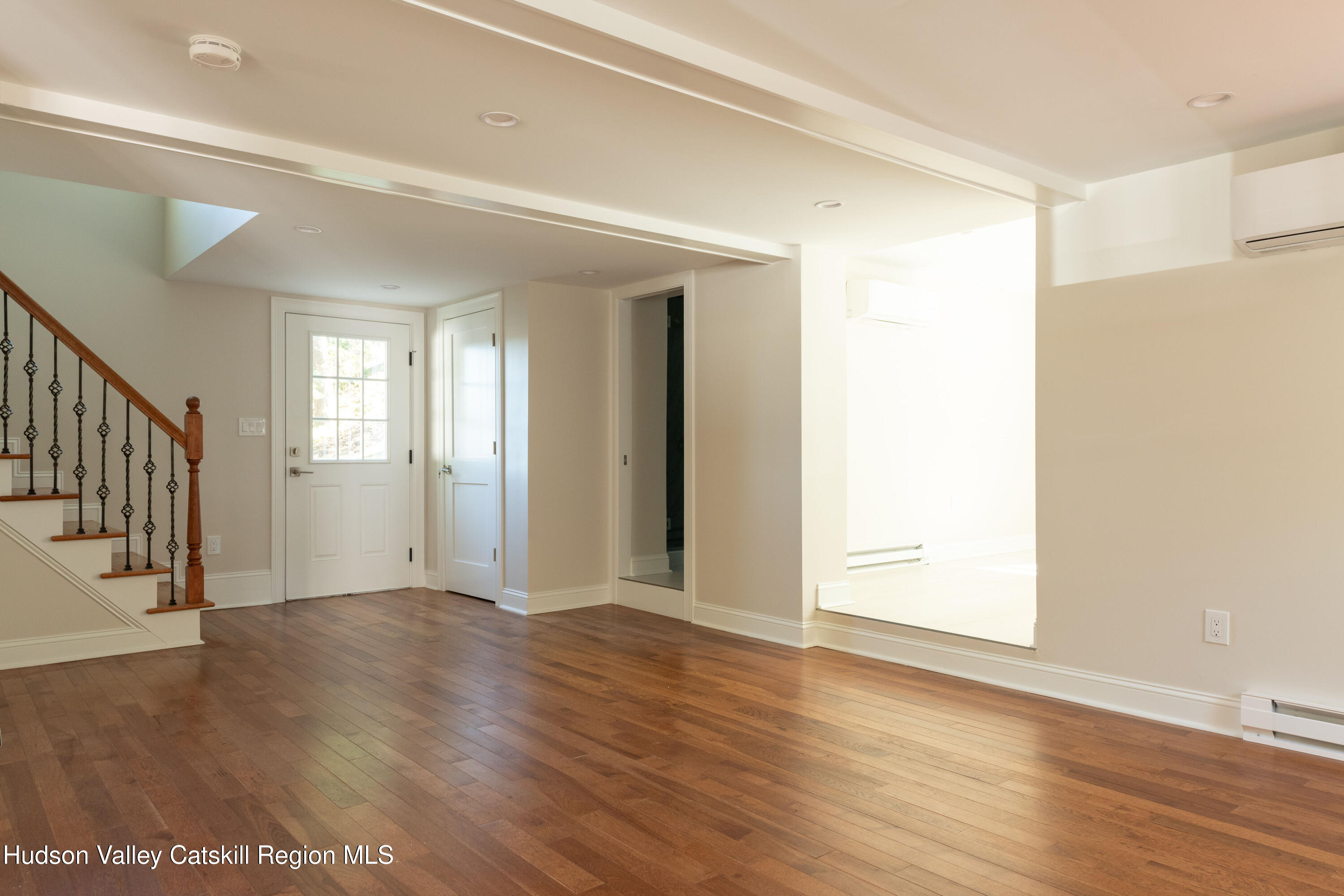 Vacant entry and living area with hardwood floors, a staircase, and a glass-paneled front door.