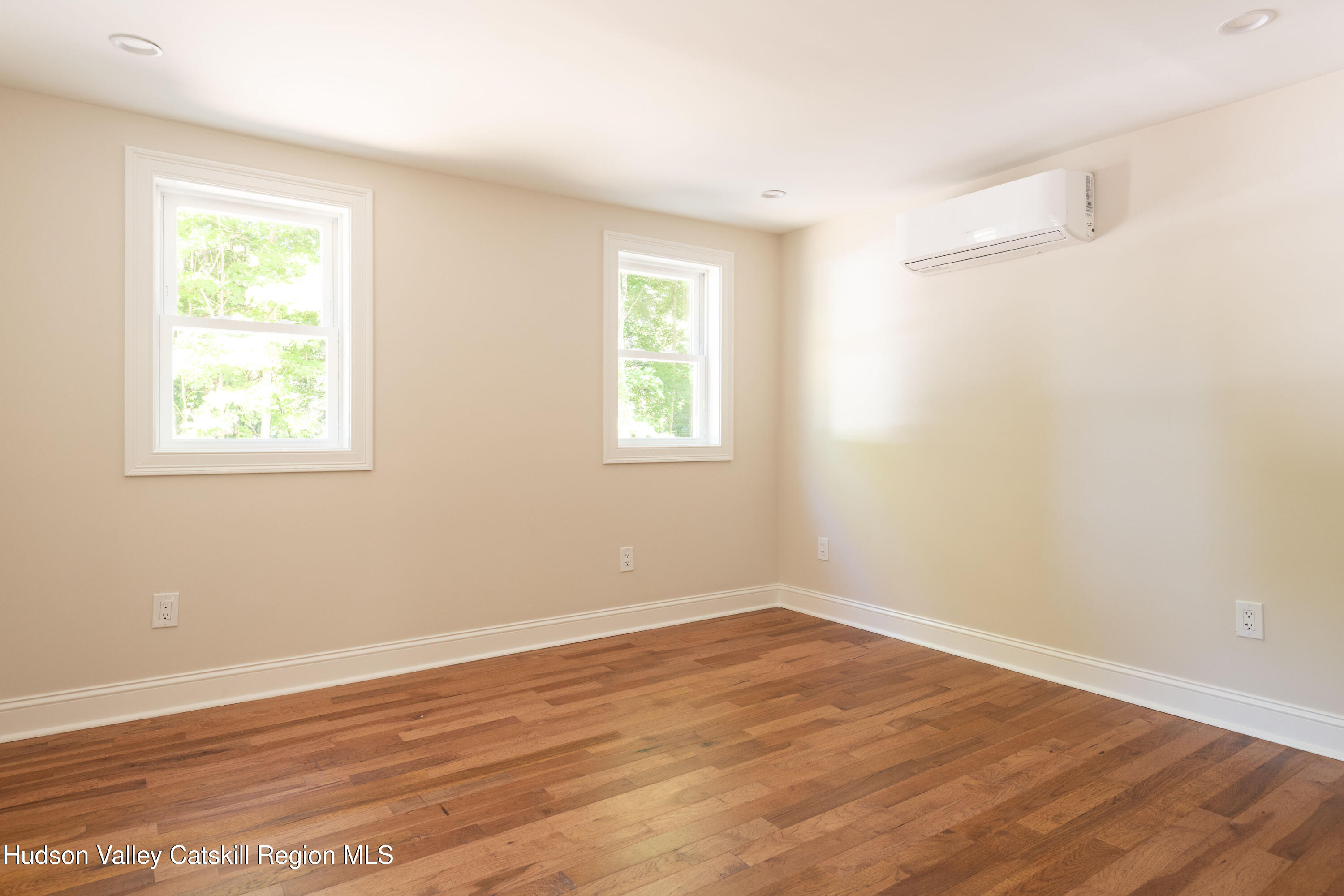 Empty room with hardwood floors, two windows, and a wall-mounted mini-split air conditioner.