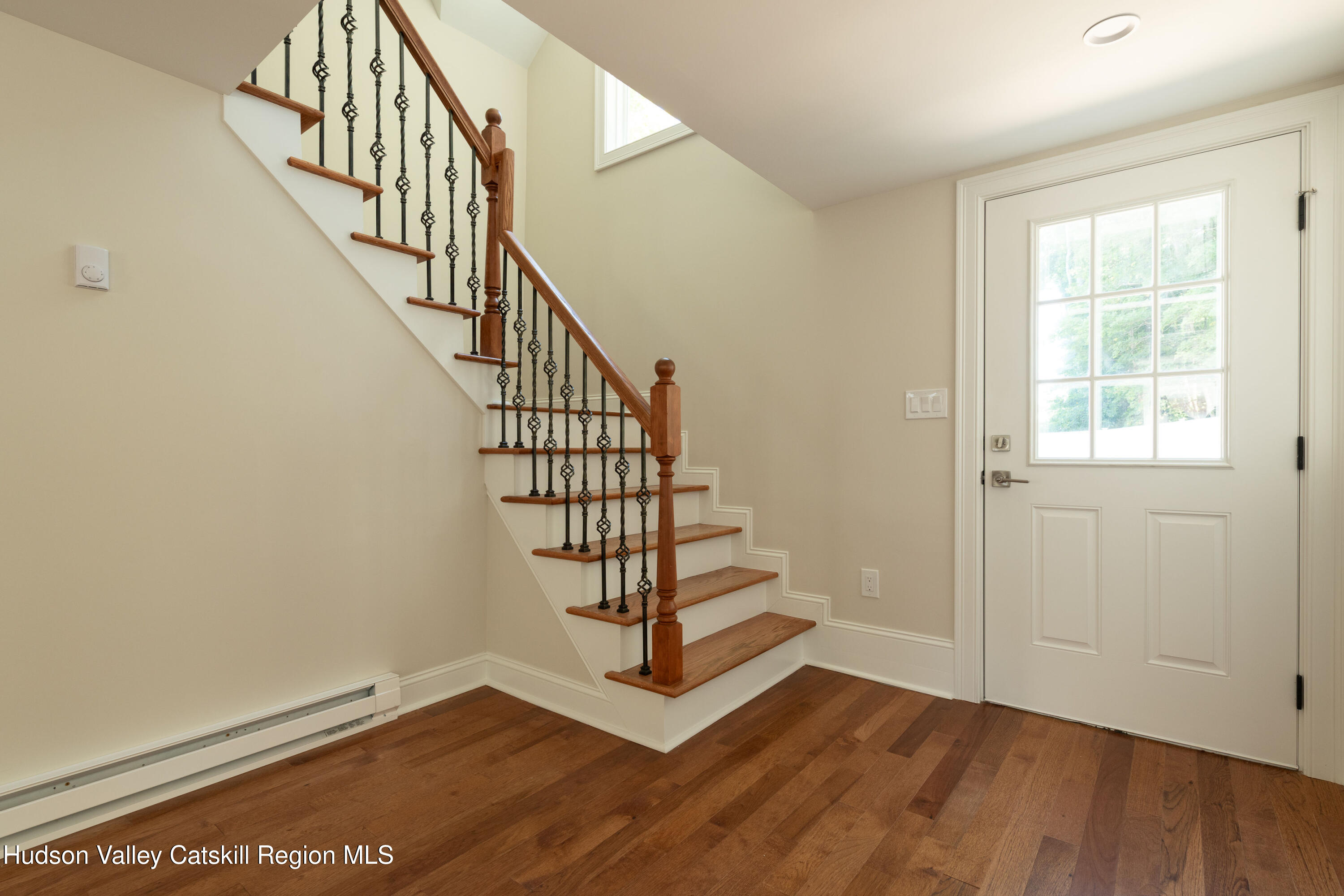 Entry hall with hardwood floors, a wood staircase with iron balusters, and a white glass-paneled front door.