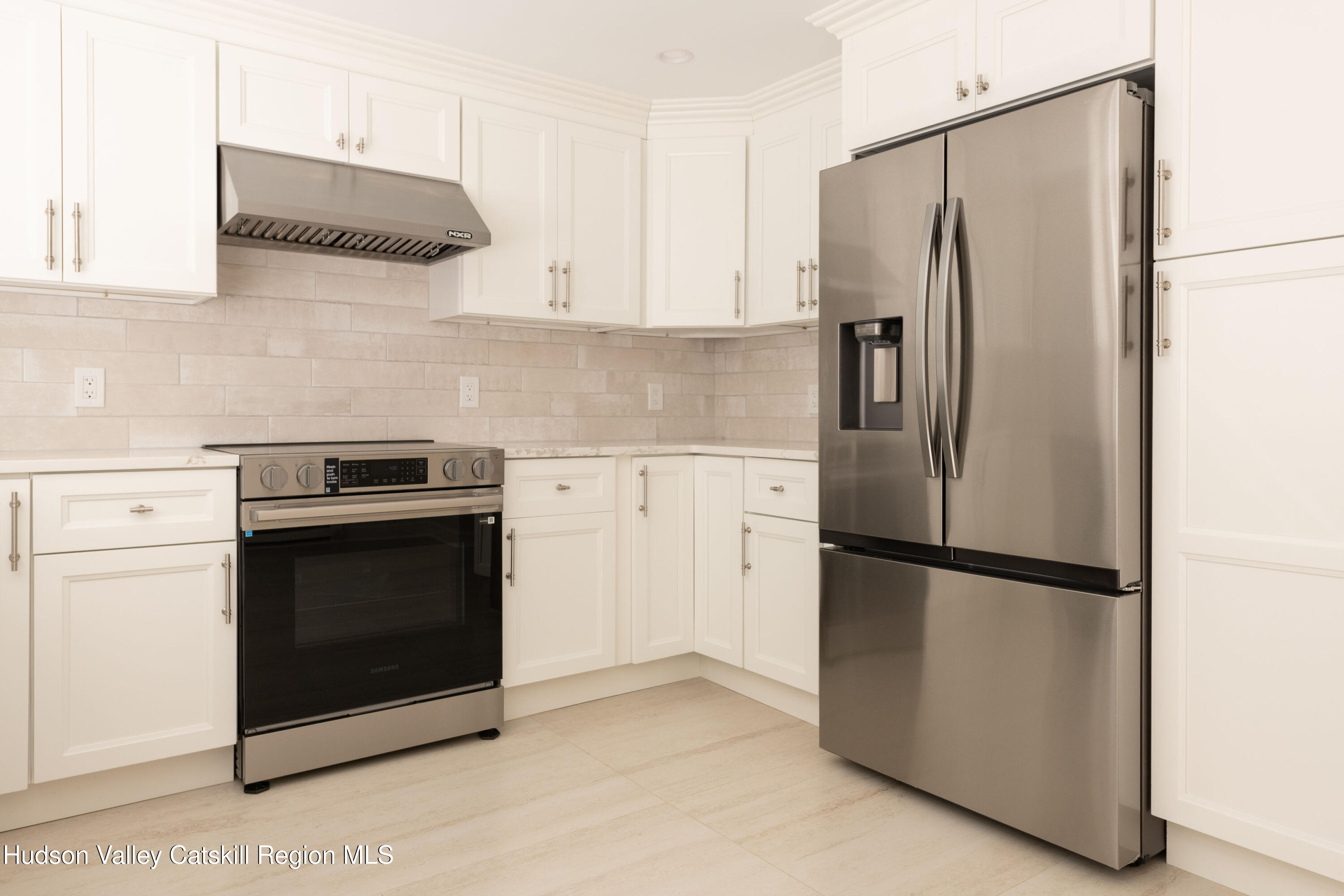 Kitchen with white shaker cabinets, pale tile backsplash, and stainless steel refrigerator and range.