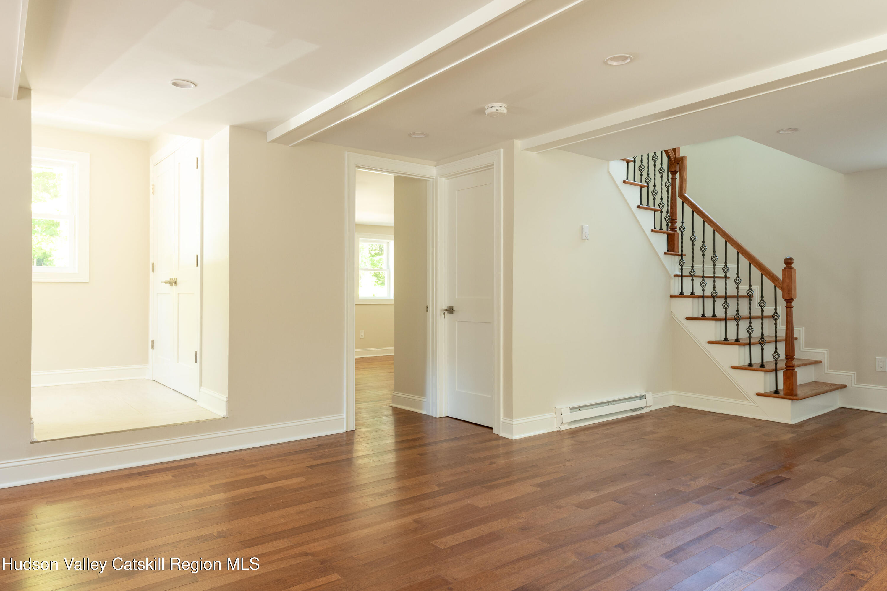 Vacant living area with hardwood floors and a wooden staircase with black iron balusters.