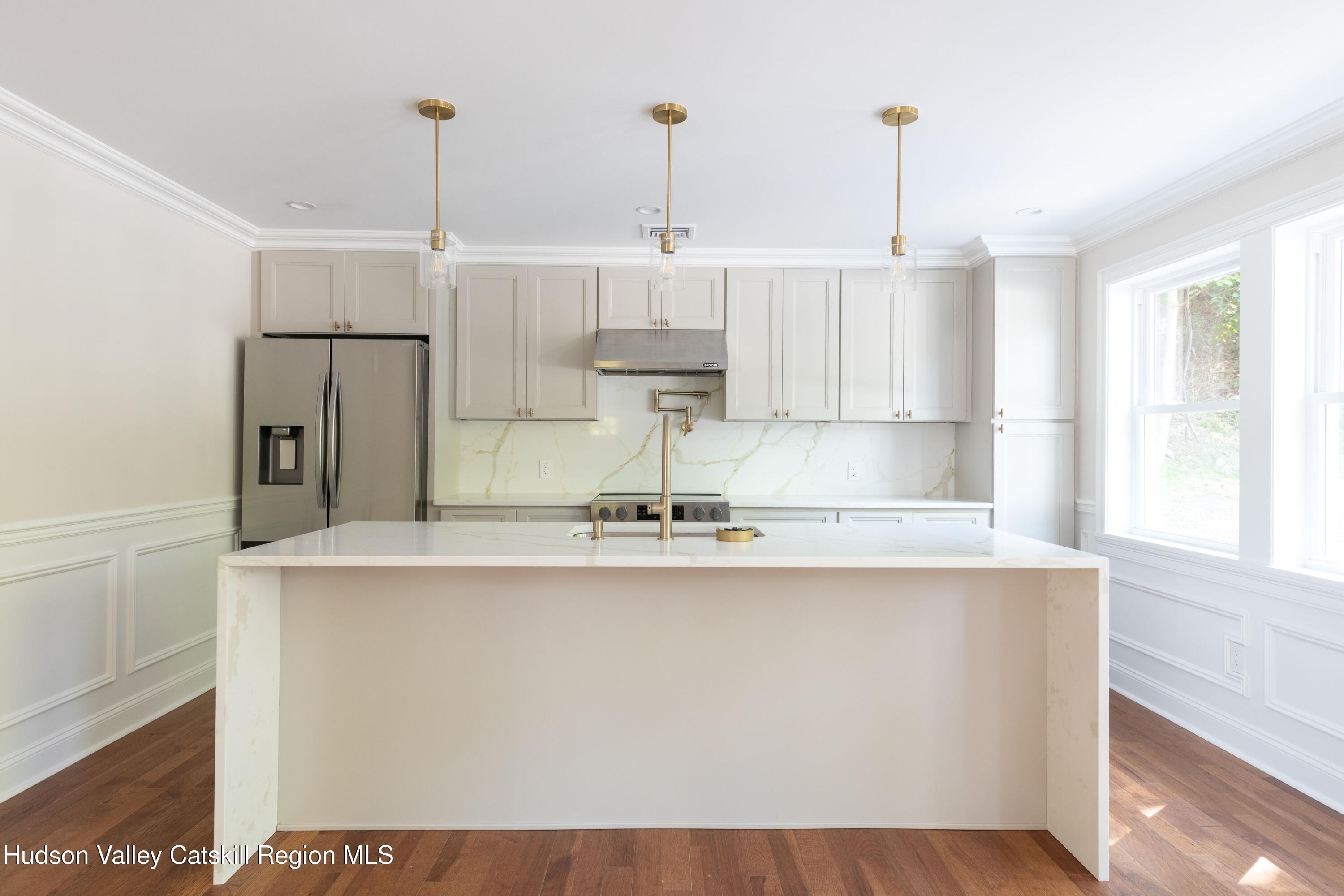 Bright kitchen with a large white waterfall island, brass fixtures, and stainless steel appliances.