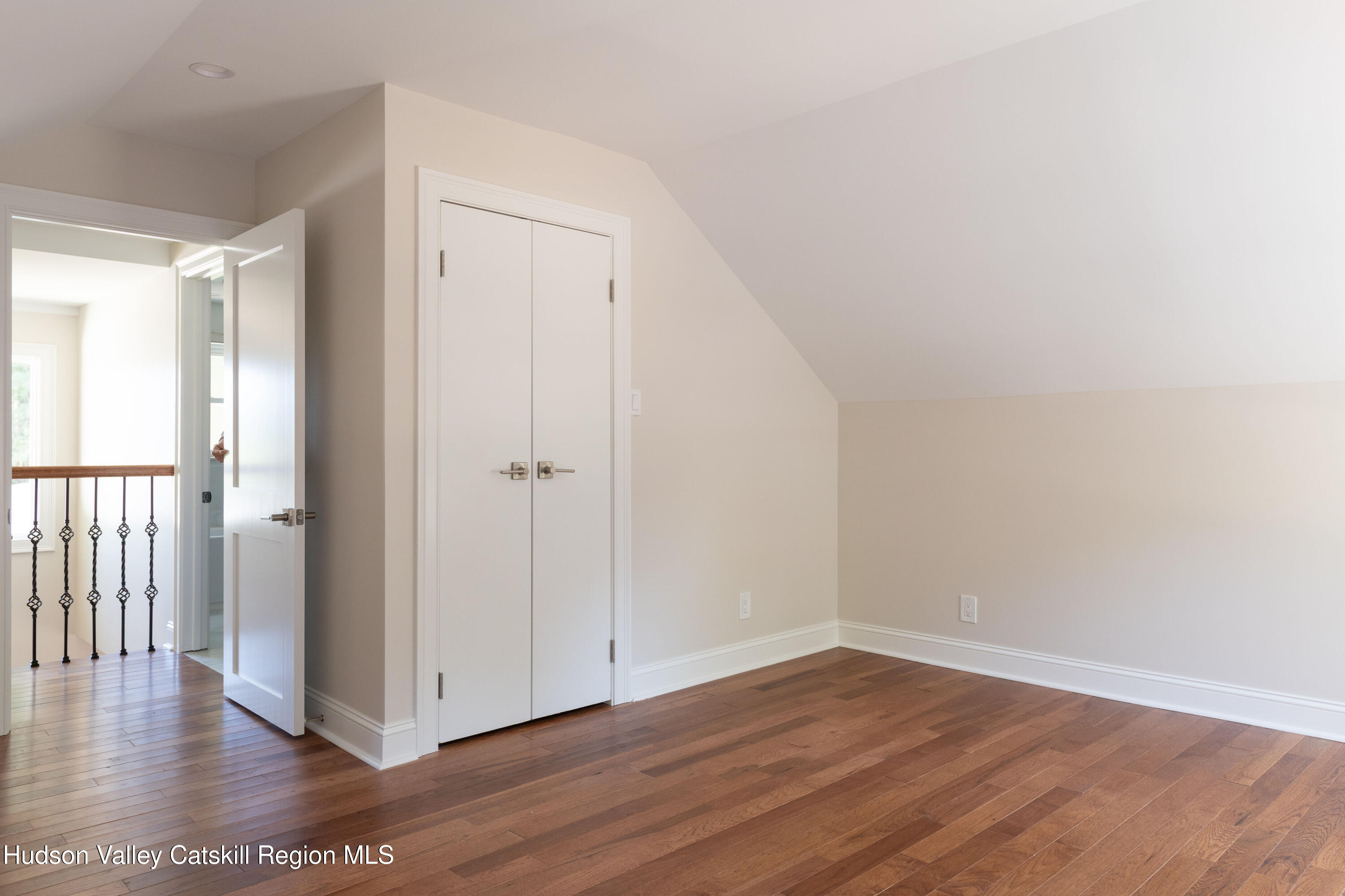 Empty room with a sloped ceiling, hardwood floors, and white double closet doors.