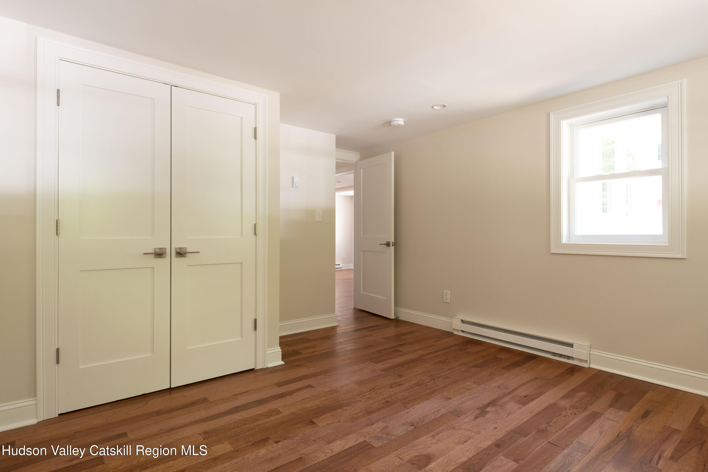 Empty room with hardwood floors, double closet doors, a window, and baseboard heating.