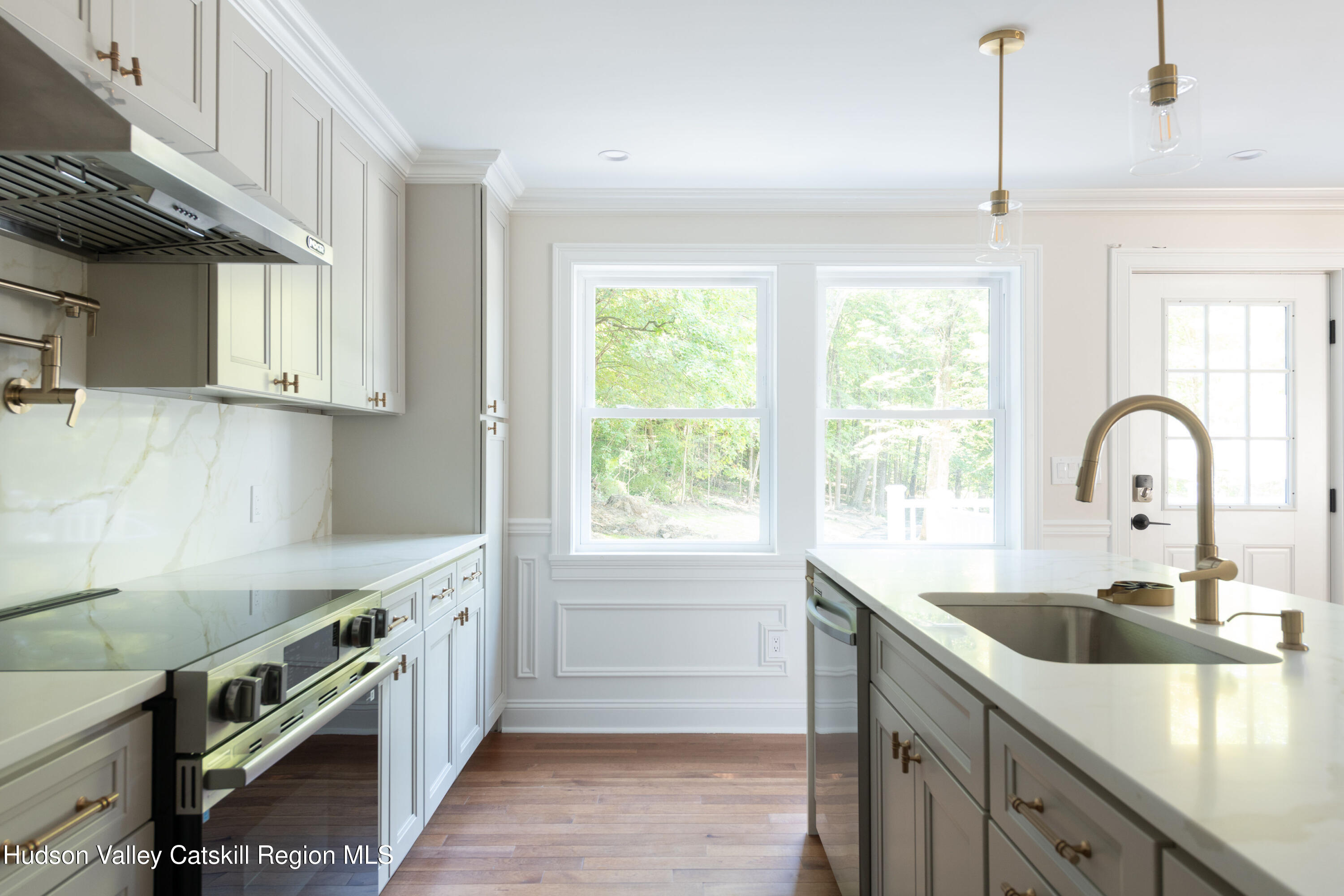 Bright white kitchen with a large island sink, stainless range, and windows overlooking trees.