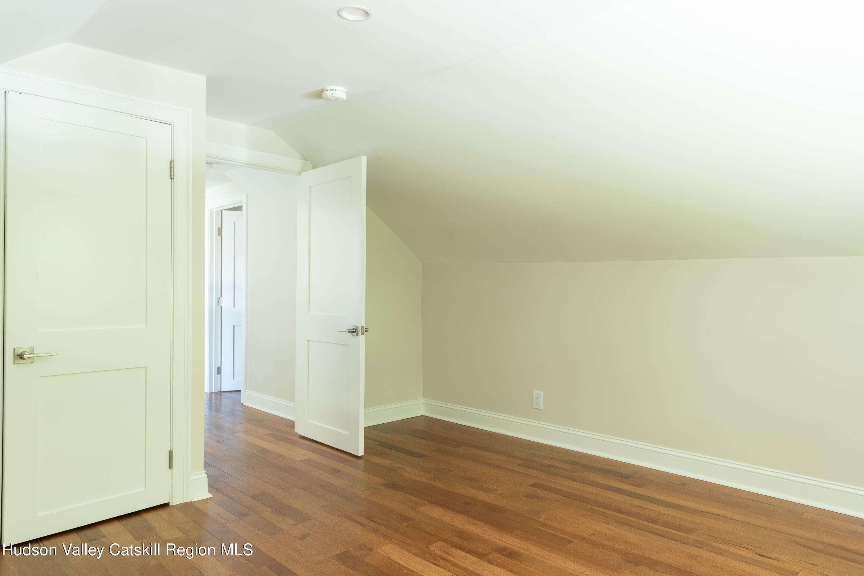 Empty room with hardwood floors, a sloped ceiling, and two open white doors.