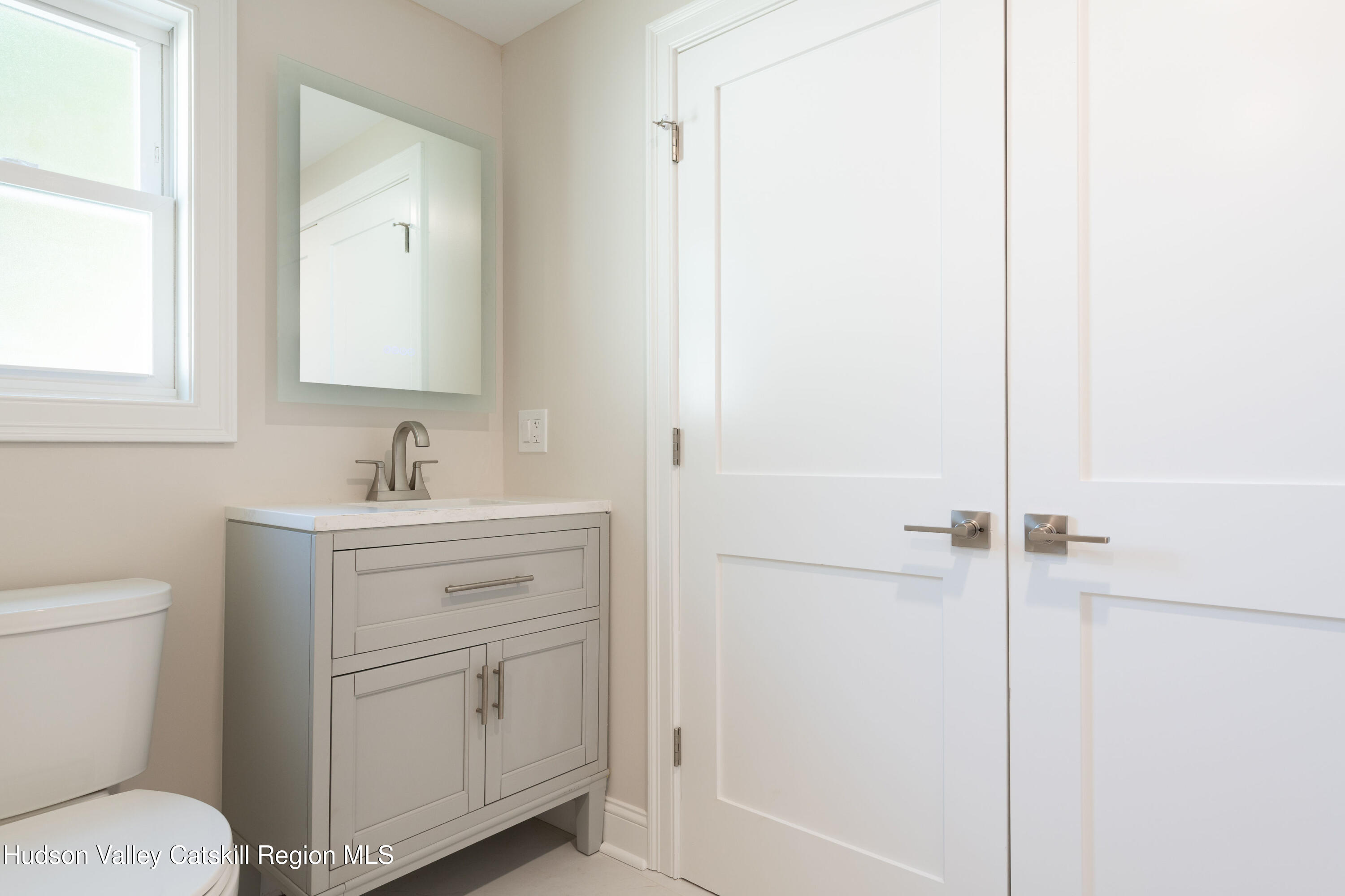 Bathroom vanity with a gray cabinet and white counter beside a toilet and paneled double doors.