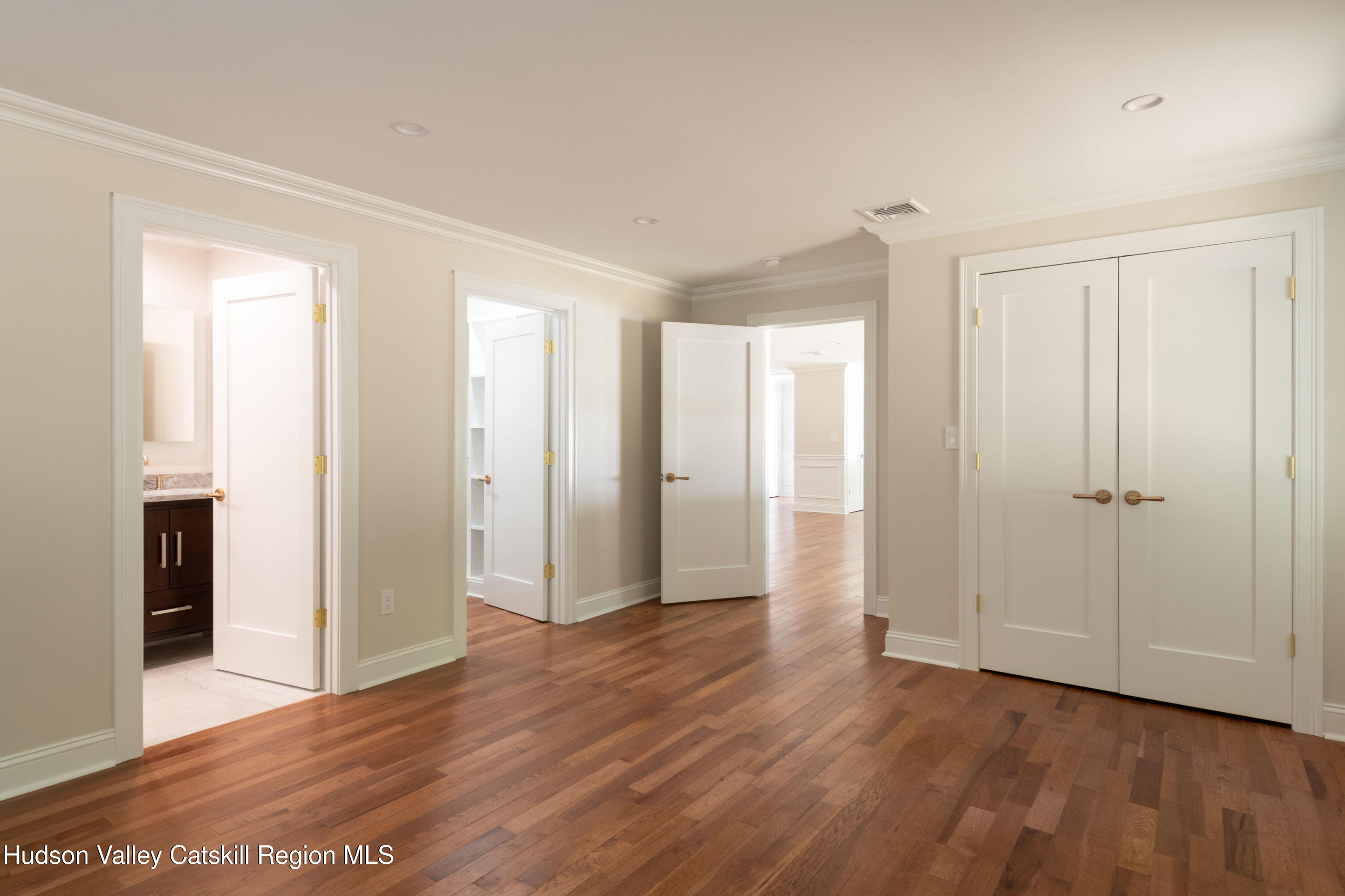 Empty room with hardwood floors, double closet doors, and open doorways to adjoining rooms.