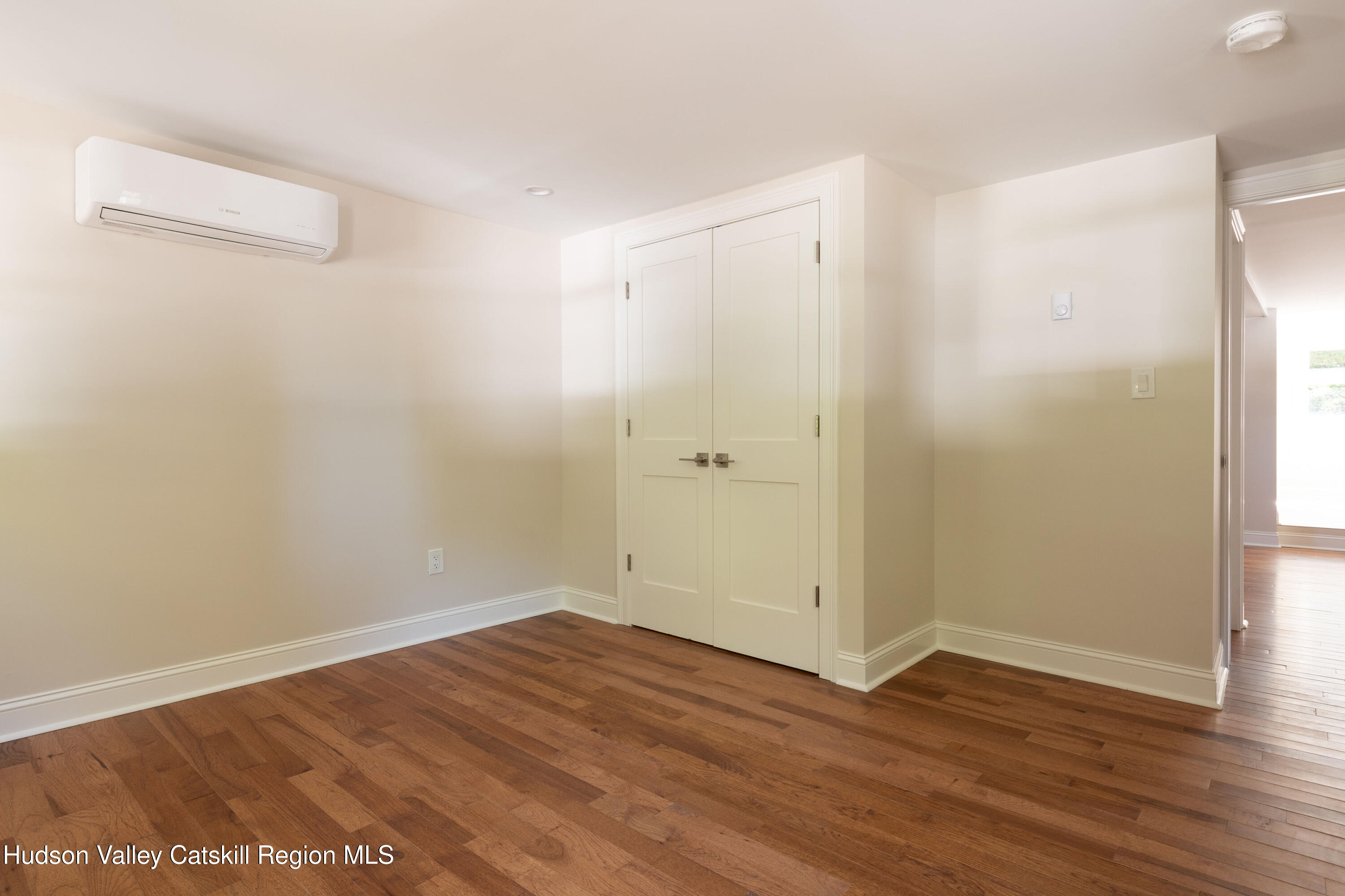 Vacant room with hardwood floors, double closet doors, and a wall-mounted mini-split.