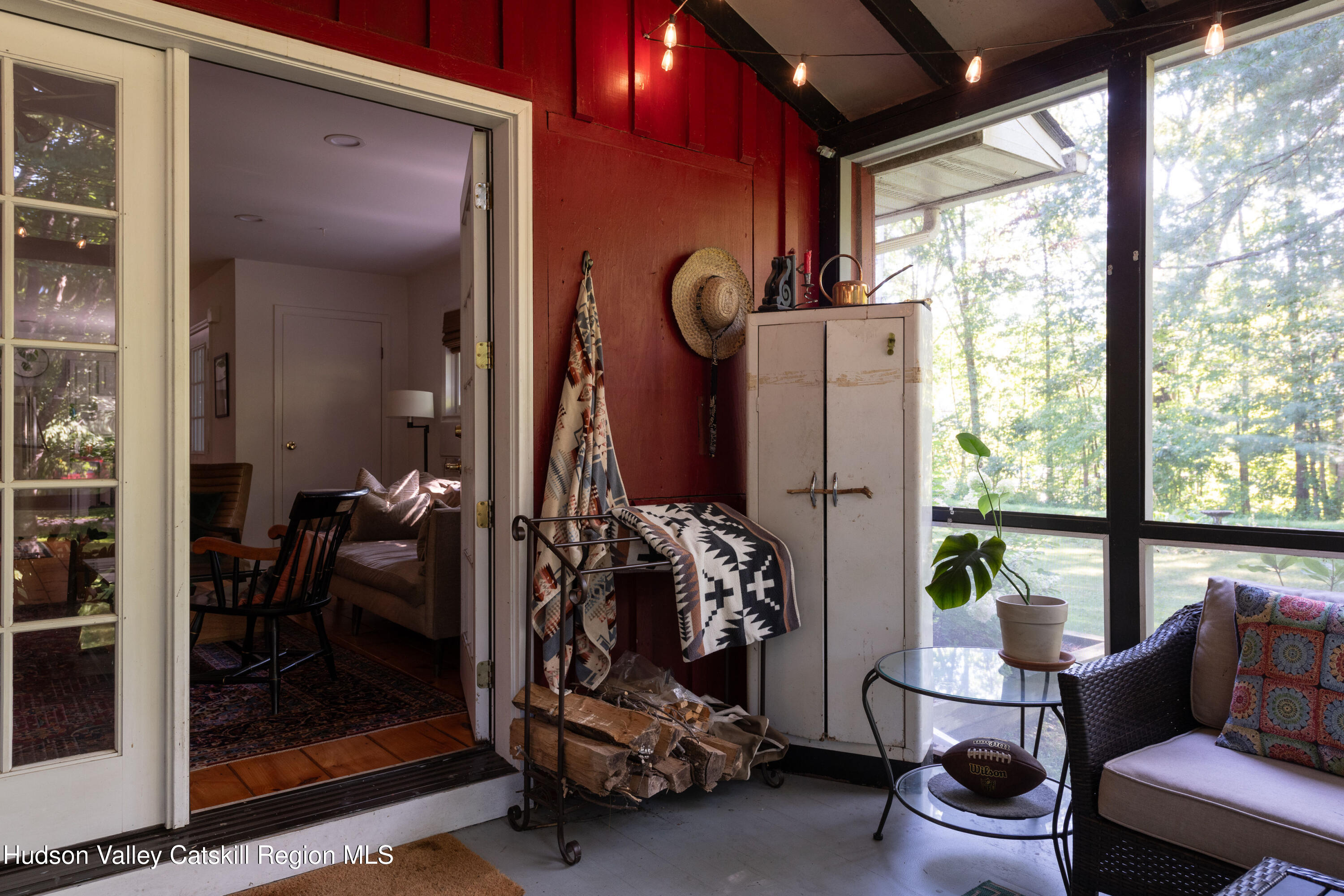 Furnished porch with red walls, wicker seating, and large windows overlooking trees.