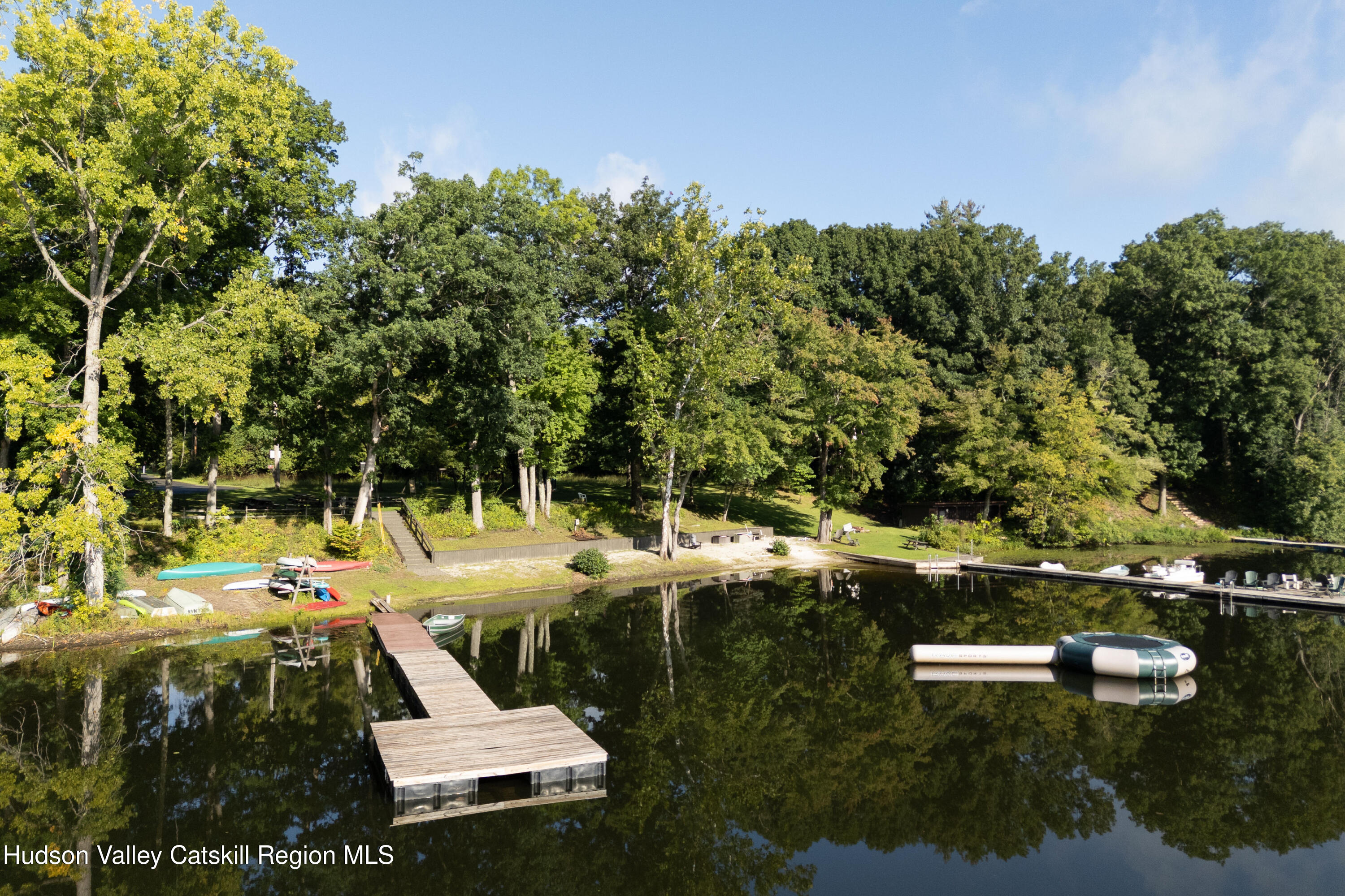 Lakefront with a wooden dock, kayaks along the wooded shore, and a floating raft.