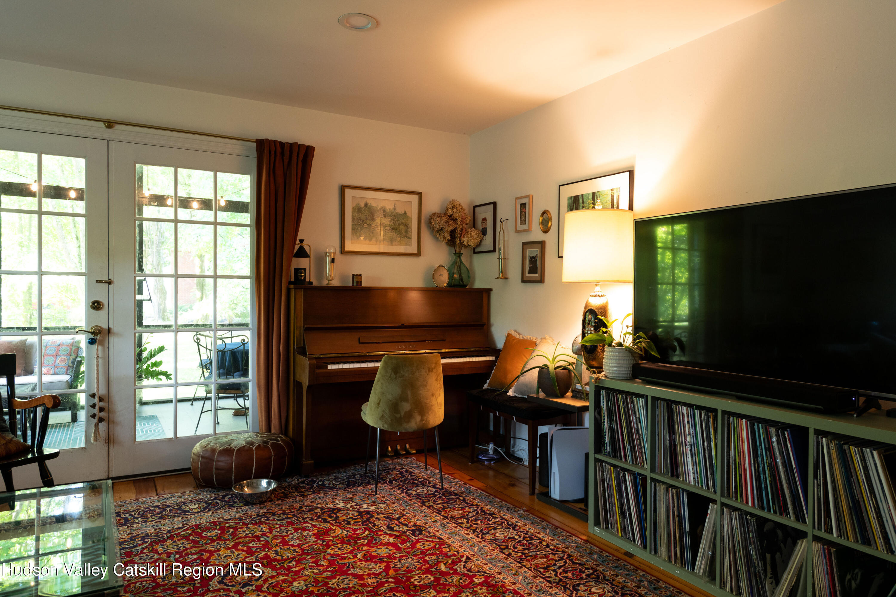 Living room with upright piano, record shelves, patterned rug, and glass doors to a patio.