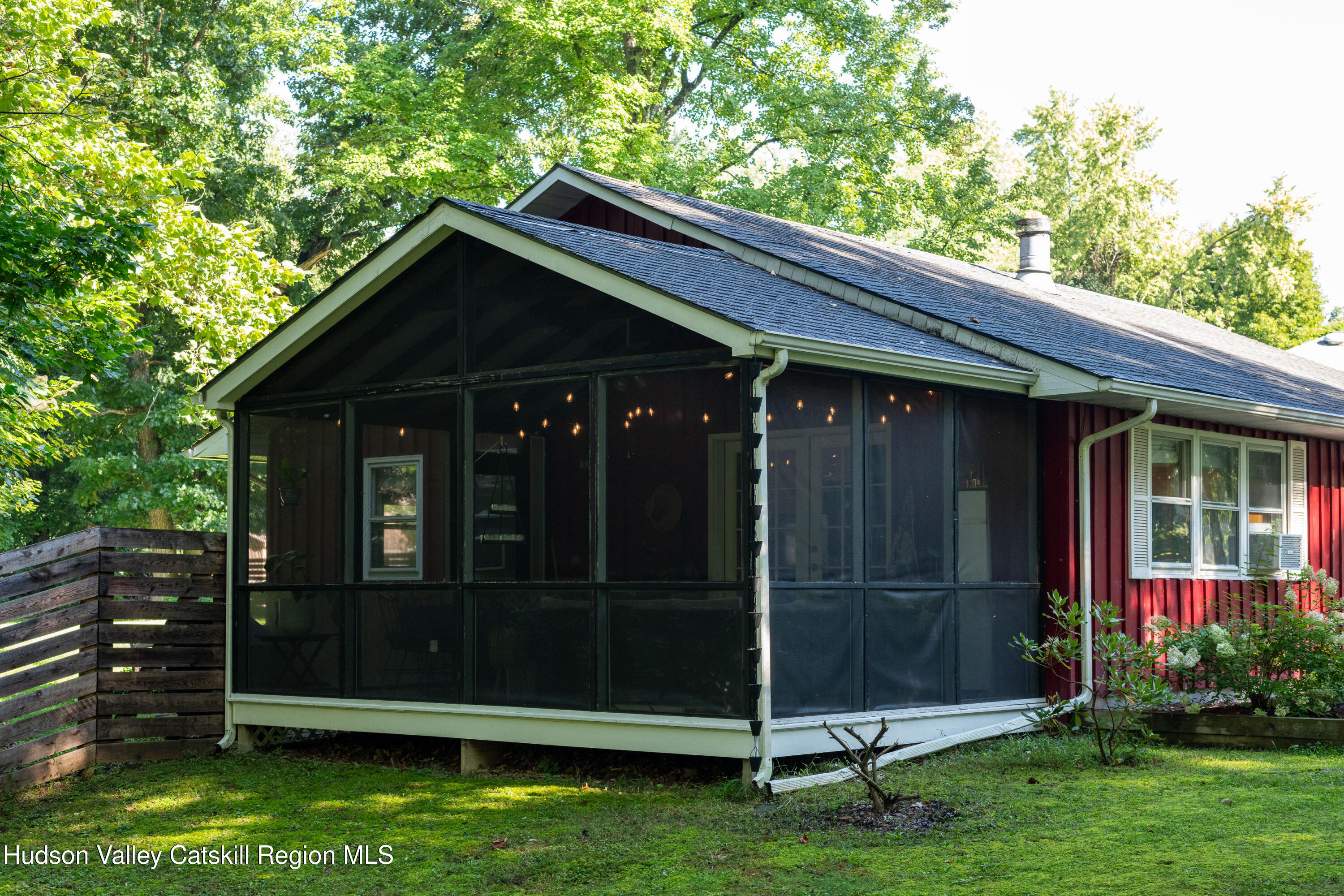 Red-sided home with a spacious screened-in porch surrounded by leafy trees.