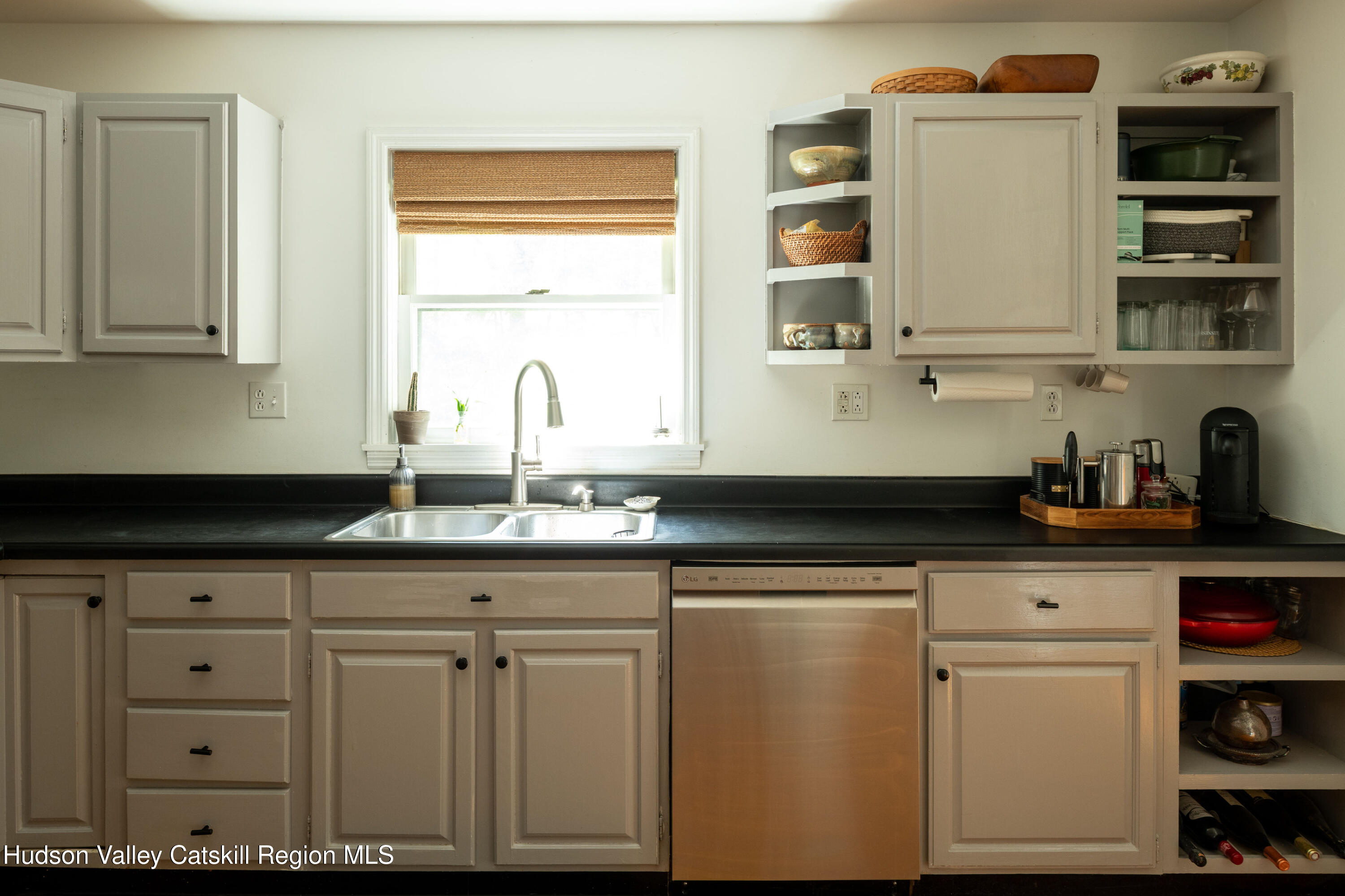 Kitchen with beige cabinets, black counters, and a double sink beneath a window with a woven shade.