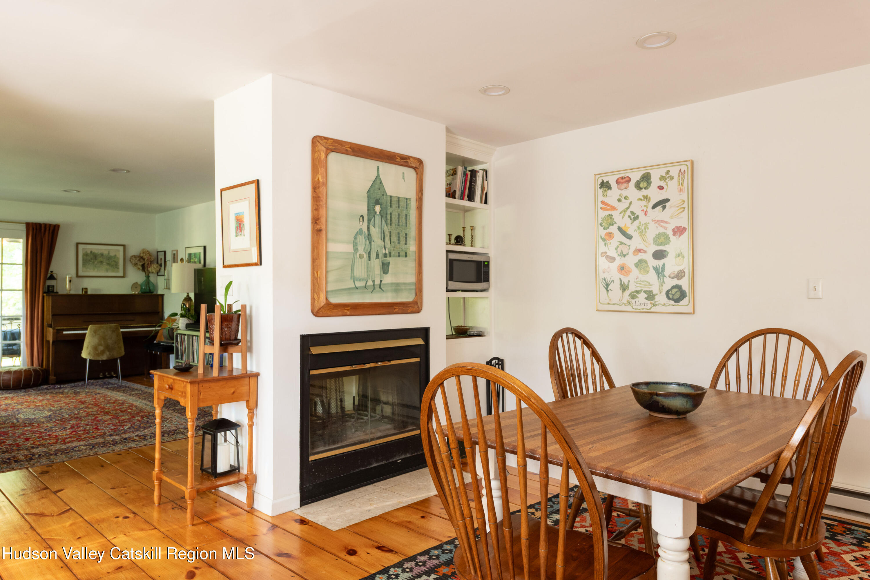 Dining room with a wooden table beside a fireplace and an adjoining living area with a piano.
