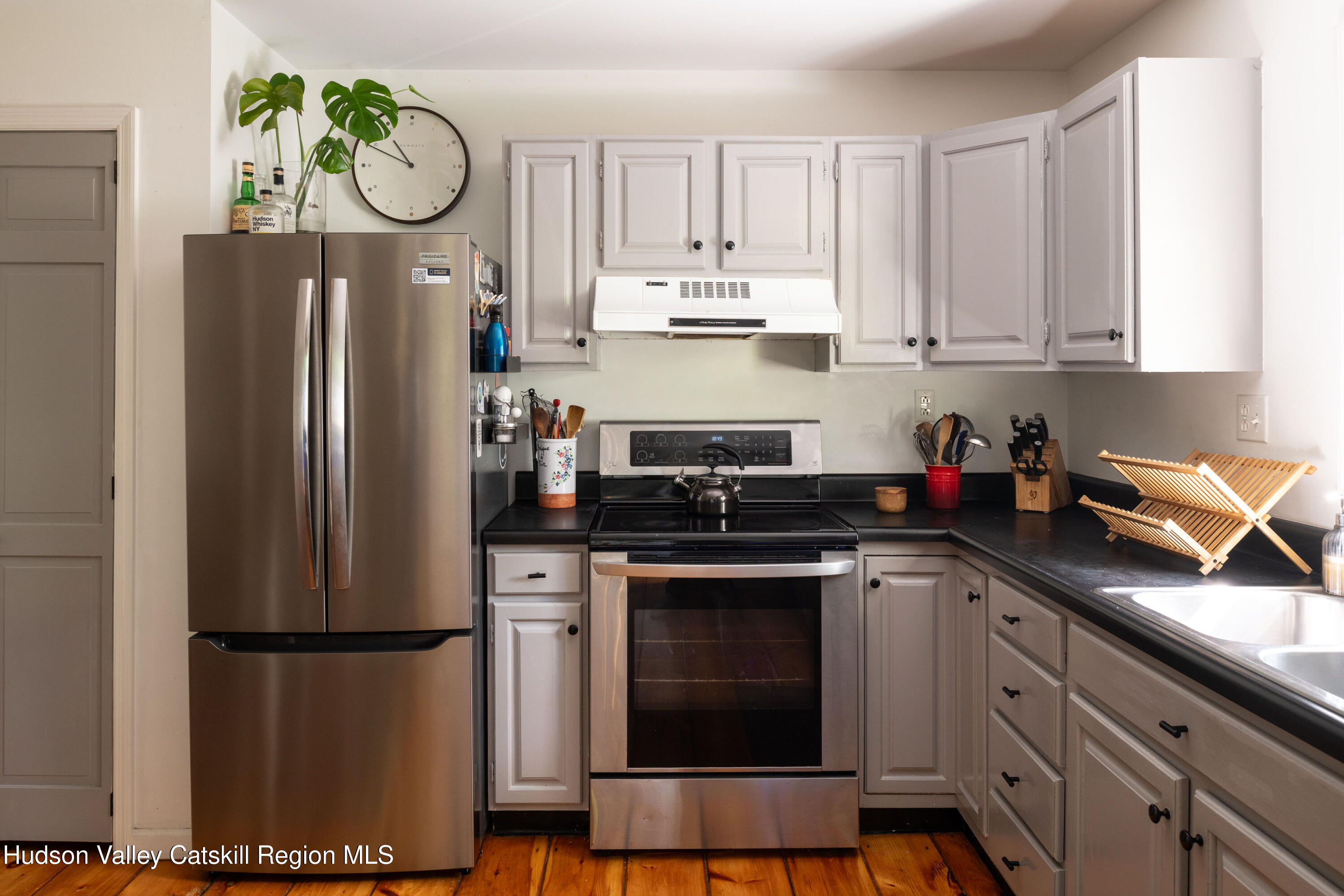Kitchen with gray cabinets, stainless steel appliances, black countertops, and wood plank flooring.
