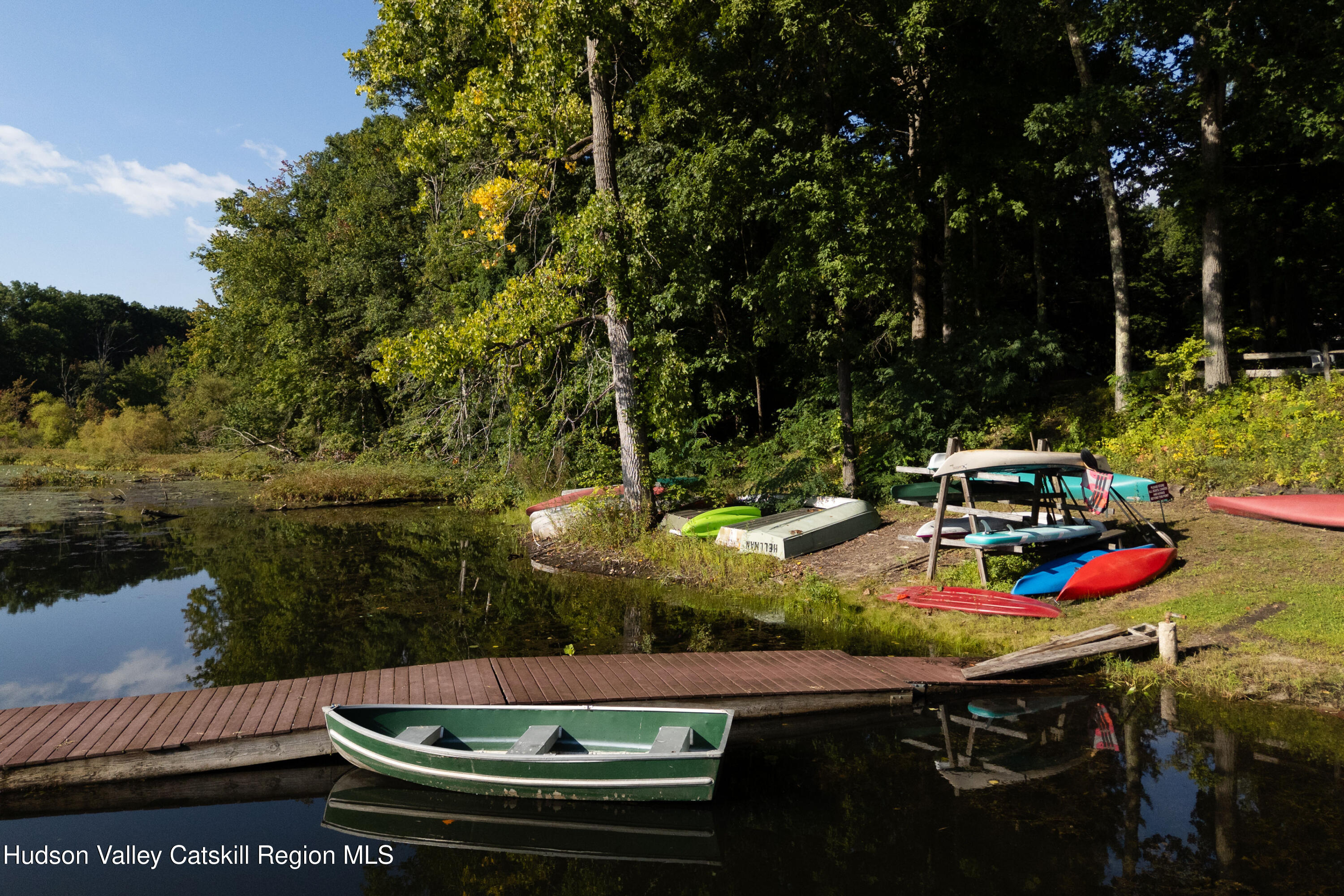 Wooded lake dock with a green rowboat in the foreground and kayaks along the shore.