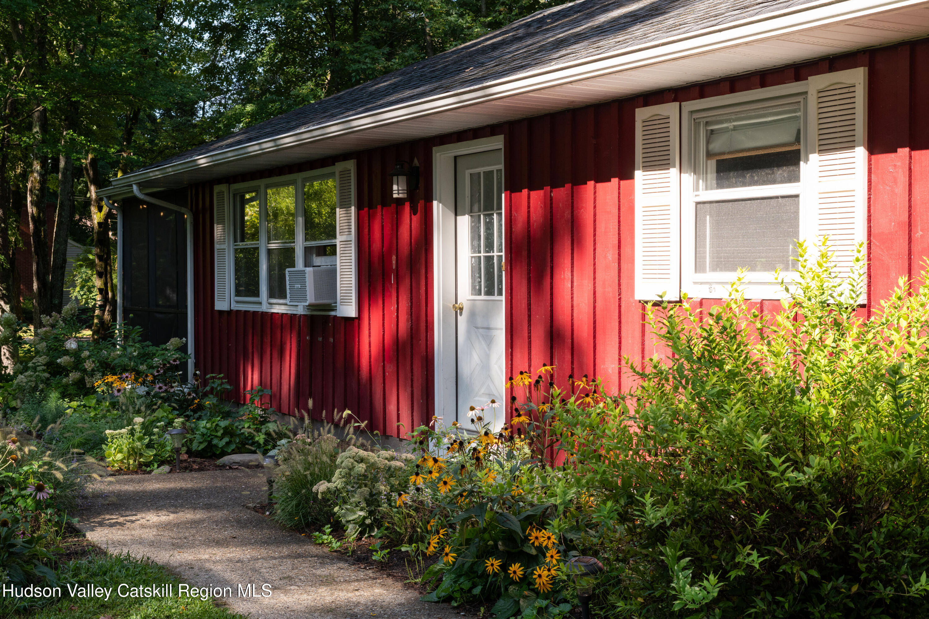 Red-sided home with white trim and a garden path bordered by flowers.