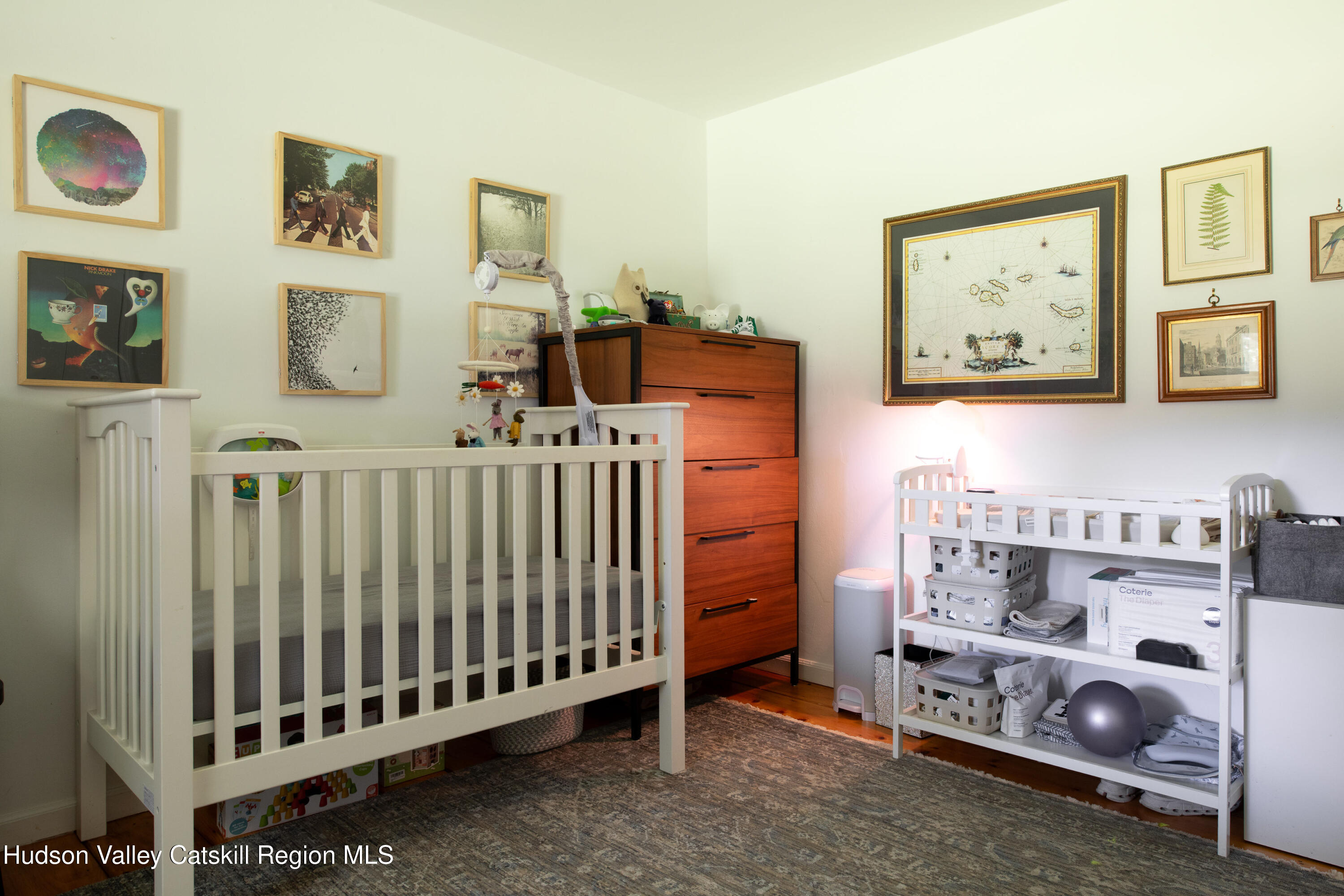 Nursery with a white crib, wooden dresser, framed artwork, and a changing shelf.