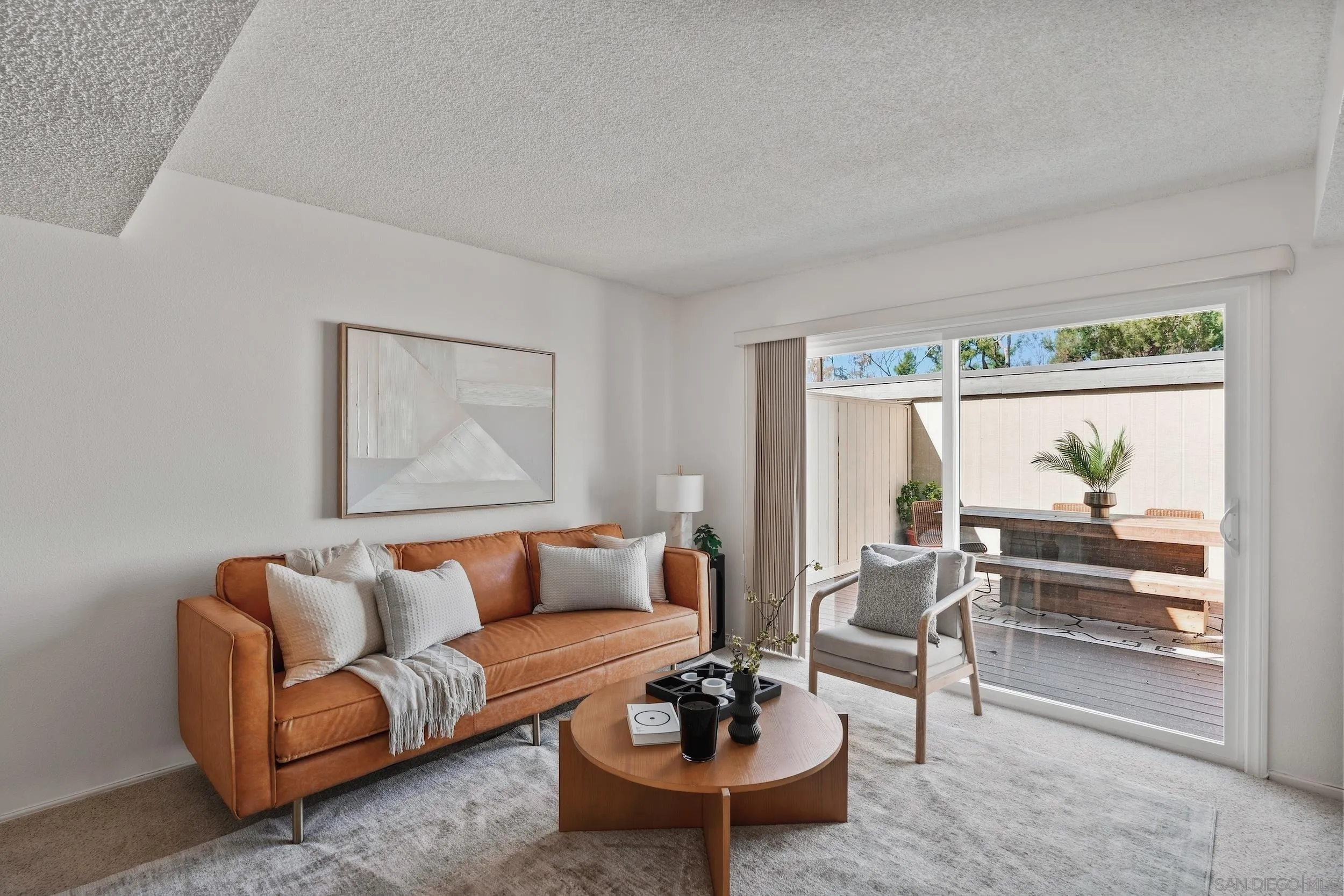 Staged living room with a tan leather sofa and sliding doors opening to a private patio.
