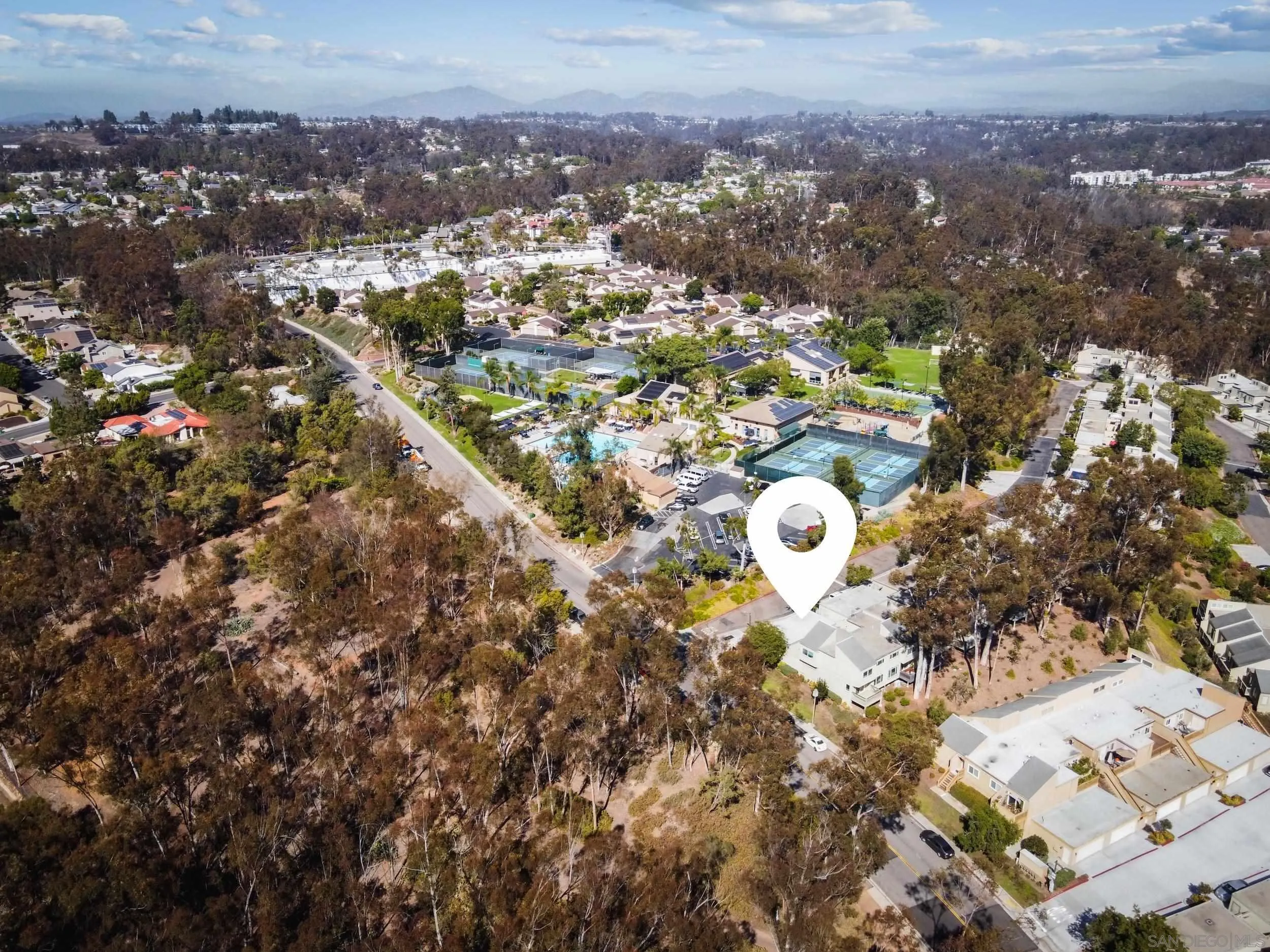 Aerial view of the home’s neighborhood, with a location marker, tennis courts, and distant mountains.